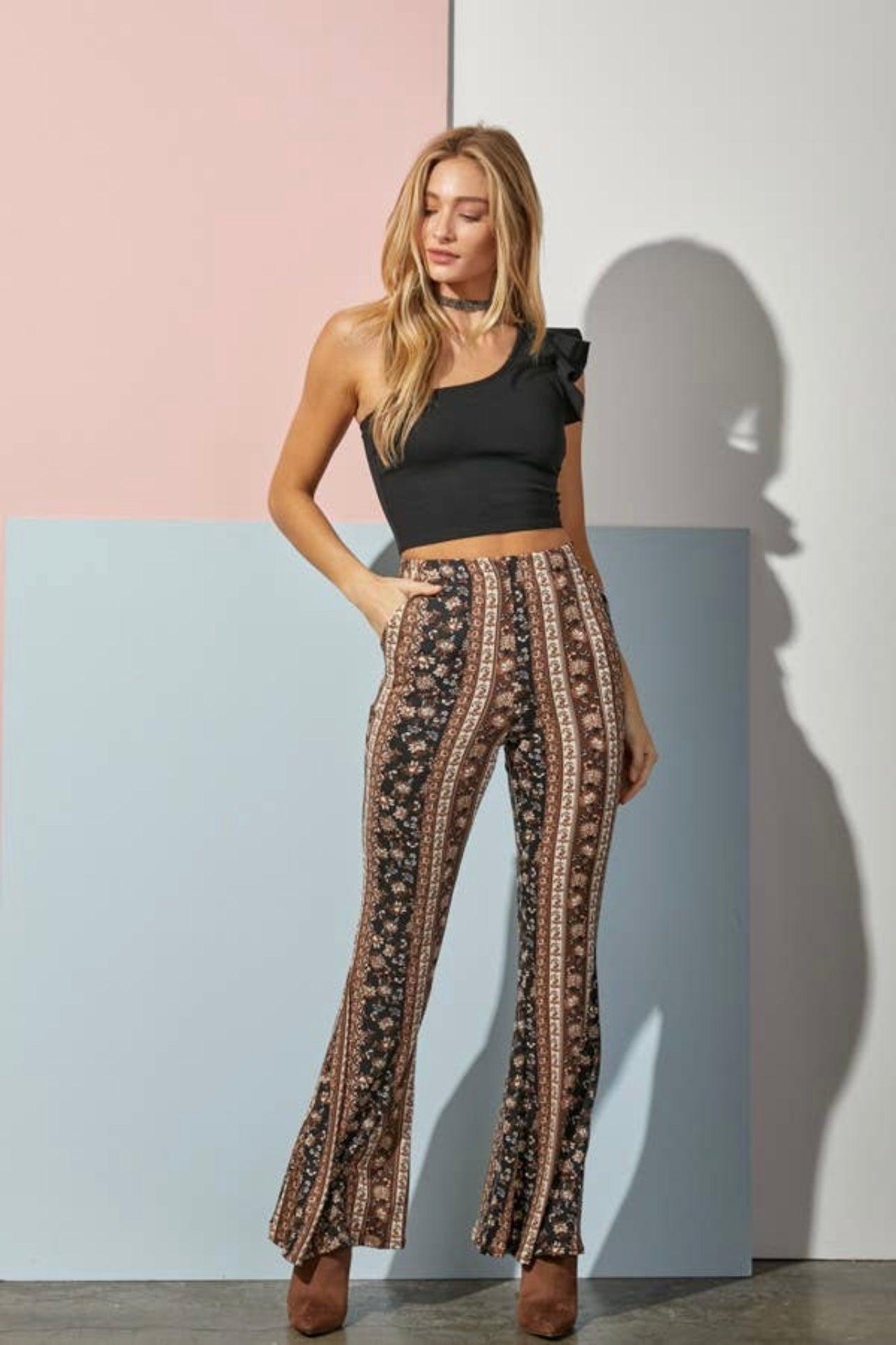 Woman wearing patterned navy and brown bell bottoms with vertical paisley stripes and black one-shoulder crop top standing against color block wall