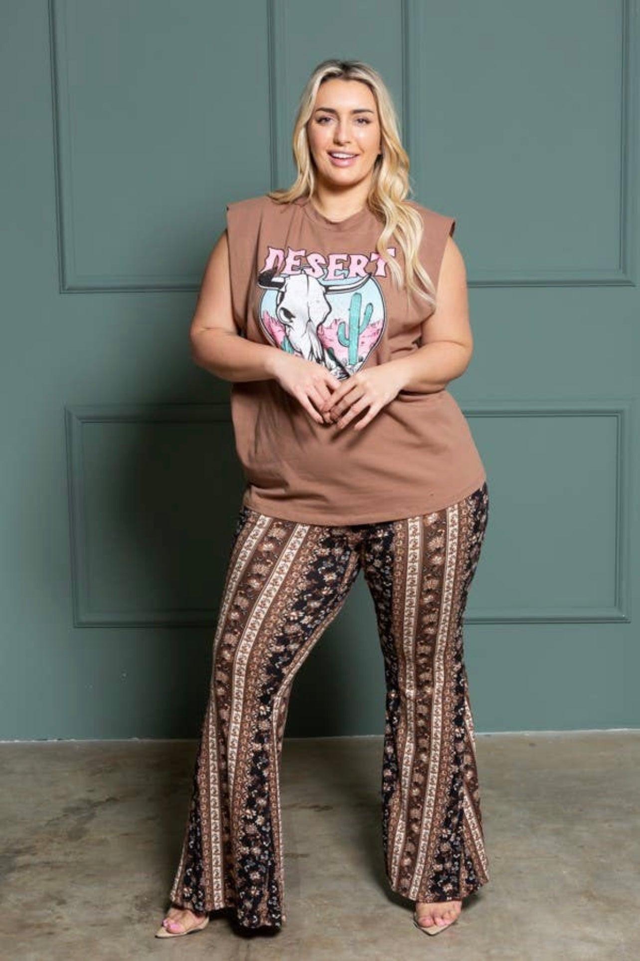 Curvy woman wearing brown graphic sleeveless top with patterned bell bottoms in navy and brown standing indoors against green wall