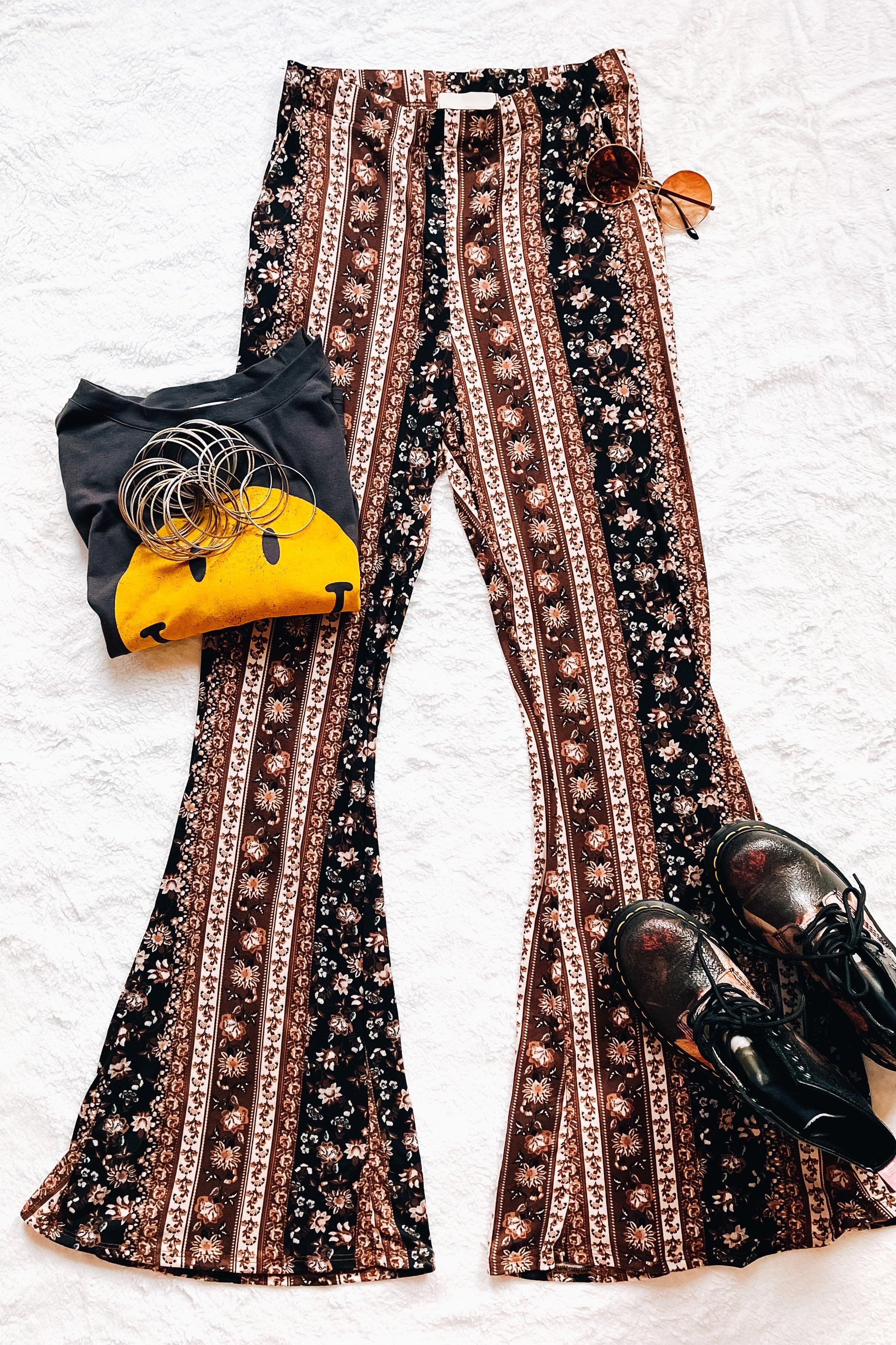 Navy and brown paisley patterned bell bottoms styled with a graphic tee, bangles, sunglasses, and black boots laid flat