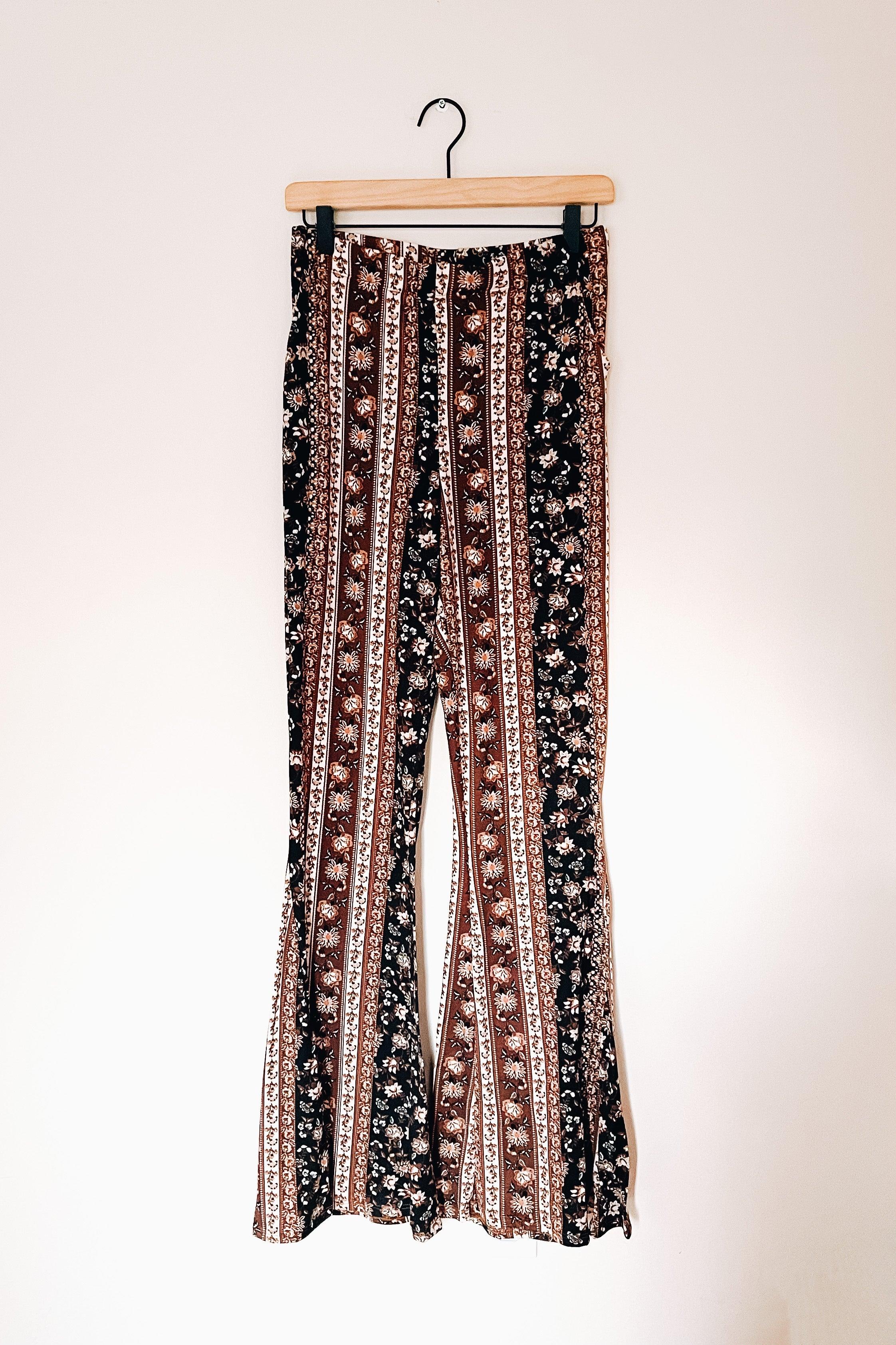 Navy and brown paisley patterned bell bottoms with vertical stripes hanging on wooden hanger against white wall