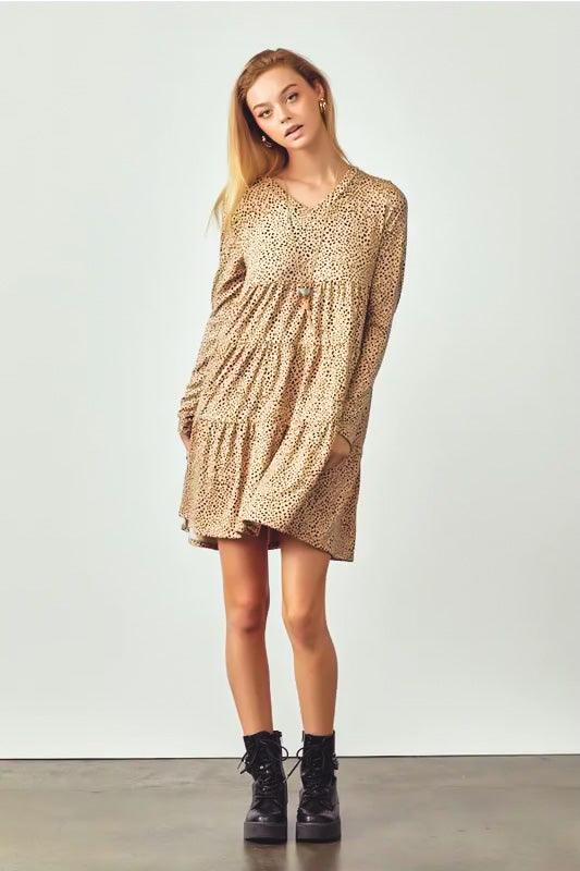Woman wearing taupe spotted long sleeve V neck dress with tiered skirt paired with black lace-up boots standing indoors