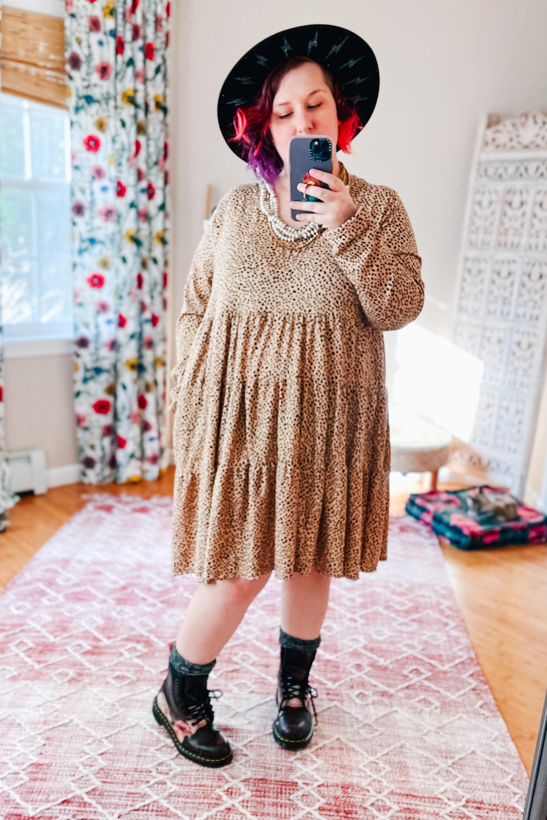 Plus size woman wearing taupe animal print V neck dress with tiered skirt and black lace-up boots indoors