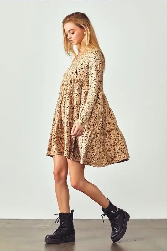 Woman wearing taupe animal print V neck dress with tiered skirt and black lace-up boots walking indoors