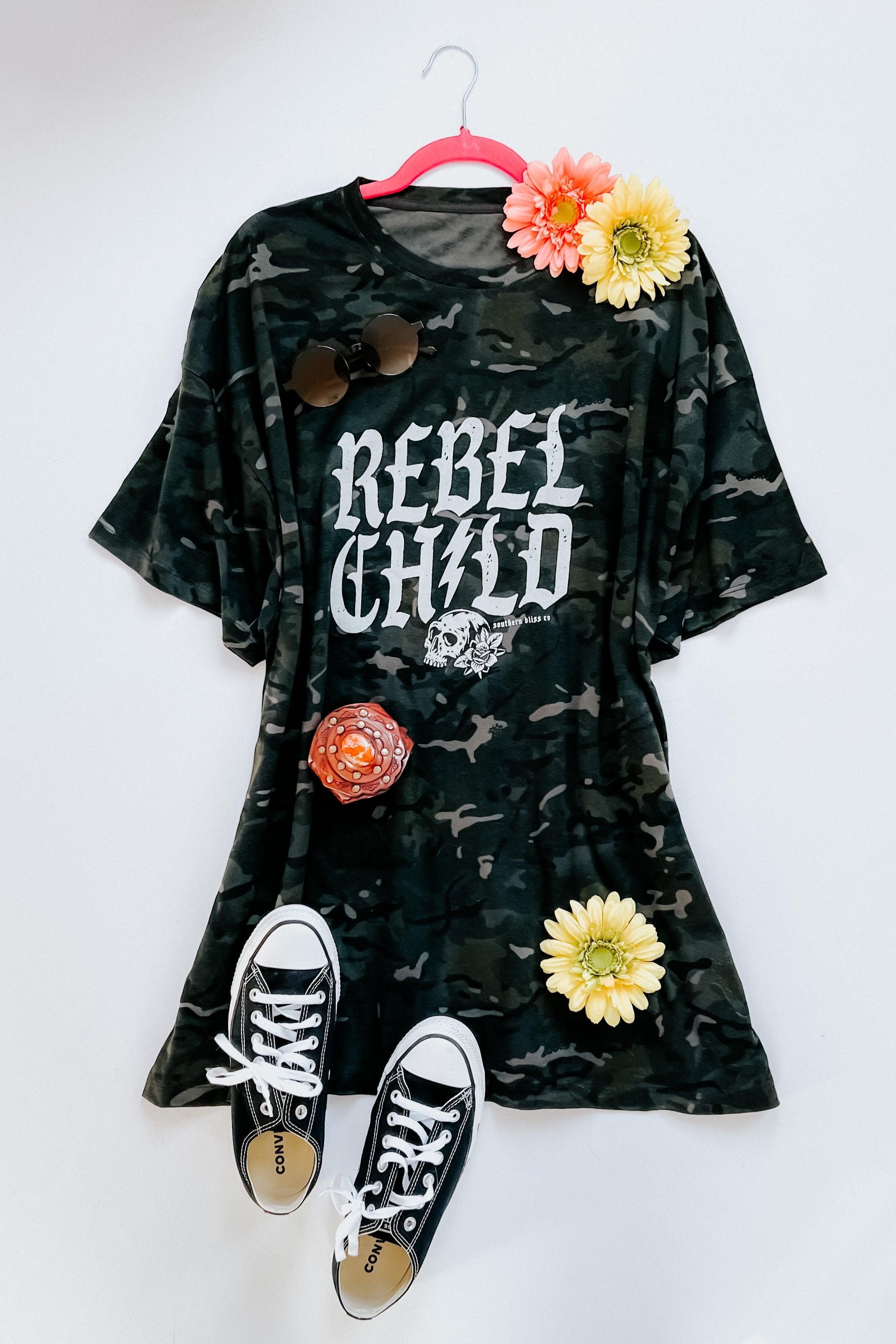 Oversized camo green tee with bold "Rebel Child" skull print styled with black sneakers and colorful flowers on hanger