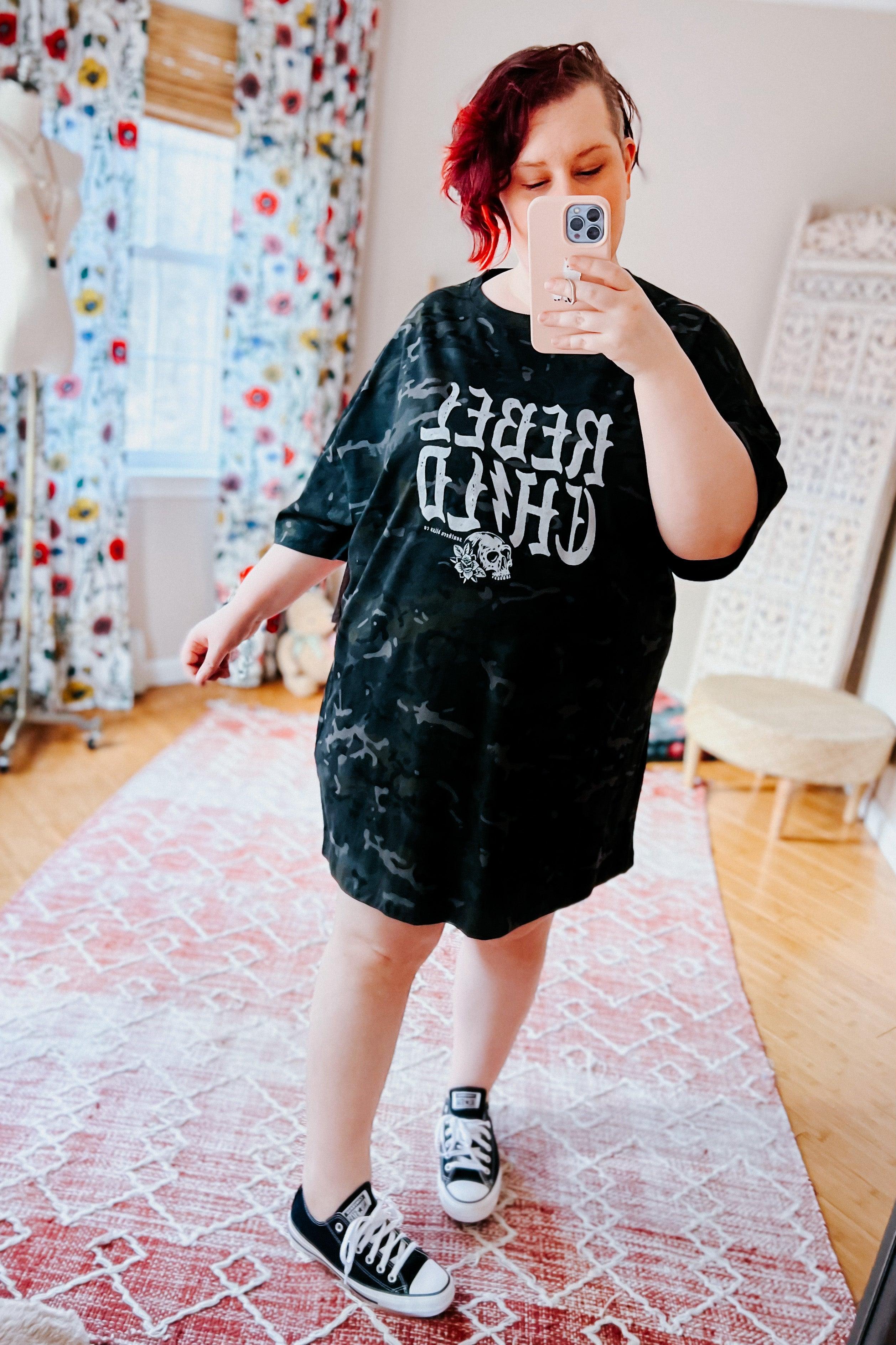 Woman wearing black camo oversized tee with reversed bold graphic and skull detail styled with black sneakers indoors