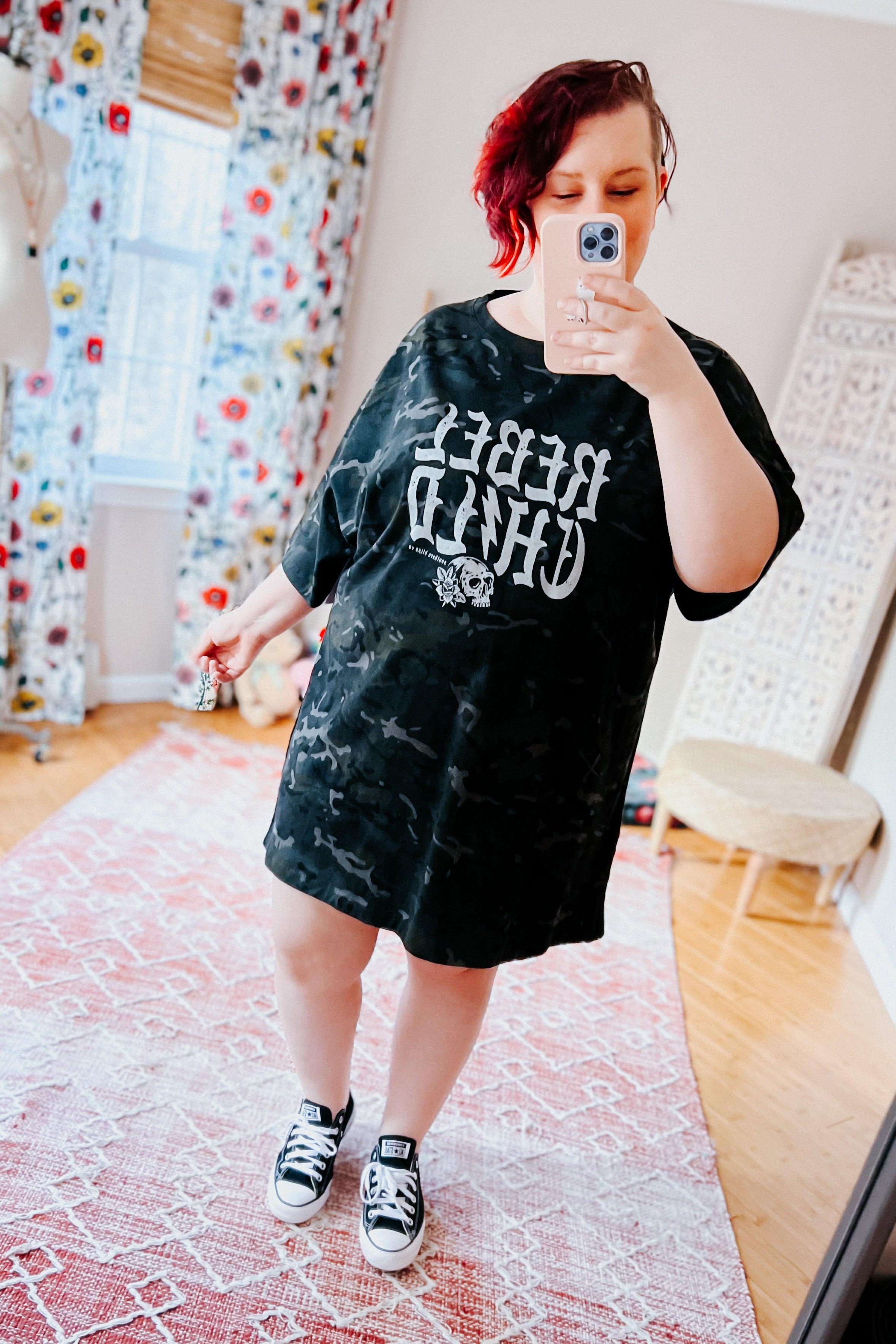 Woman wearing black camo oversized tee with bold reversed skull graphic styled with casual sneakers indoors