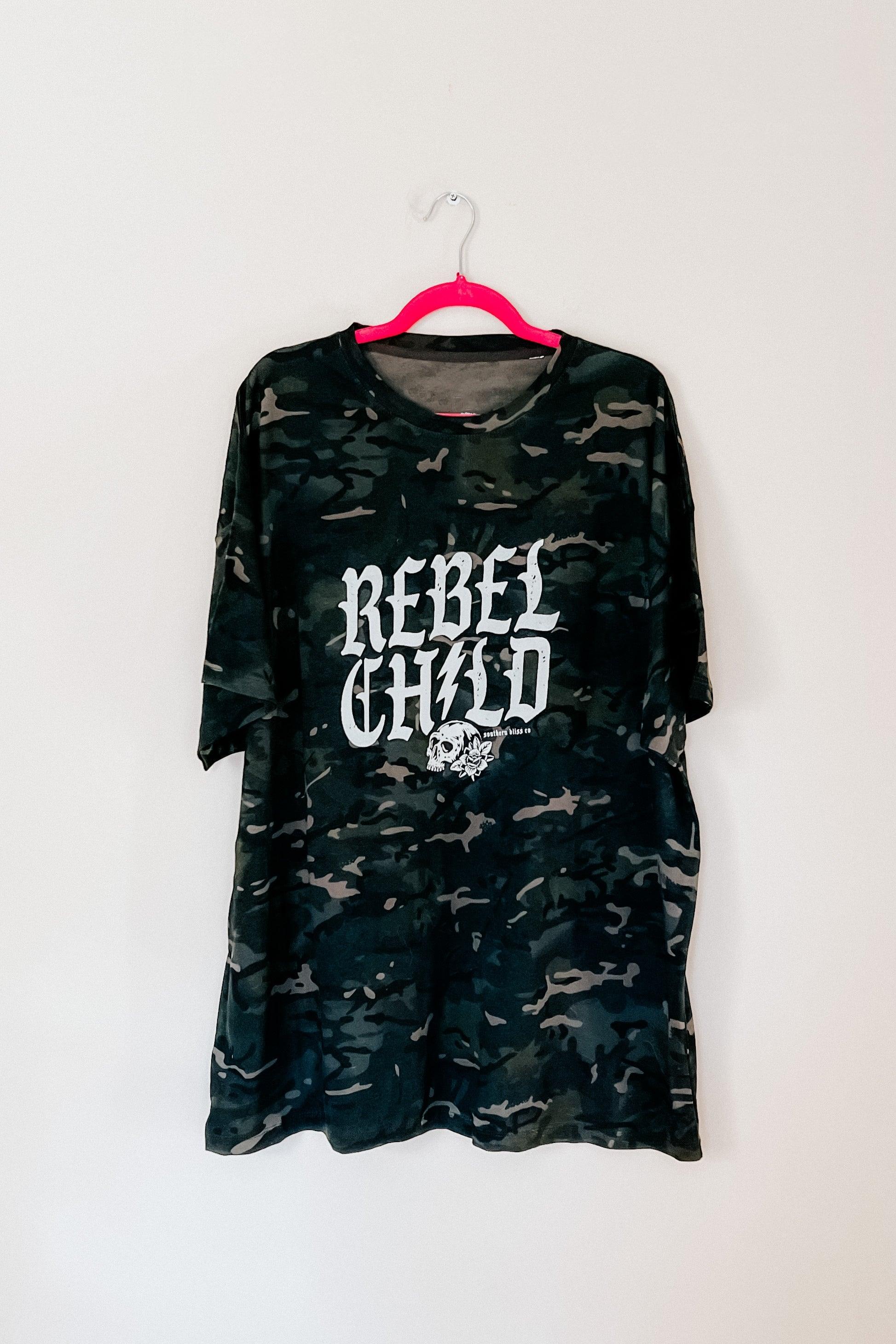 Camo green oversized tee with bold “Rebel Child” skull graphic hanging on bright pink hanger against white wall