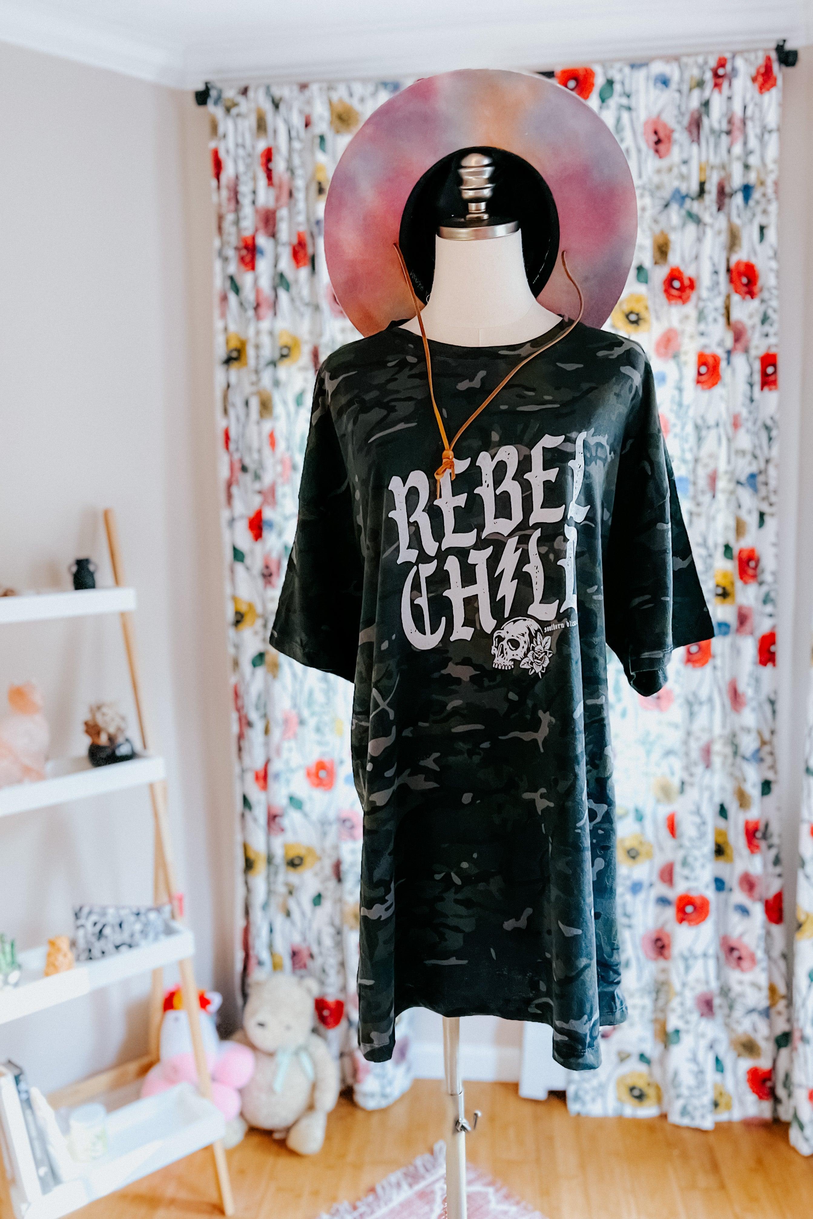 Mannequin dressed in oversized camo green tee with bold skull graphic, accessorized with pendant necklace in bright room