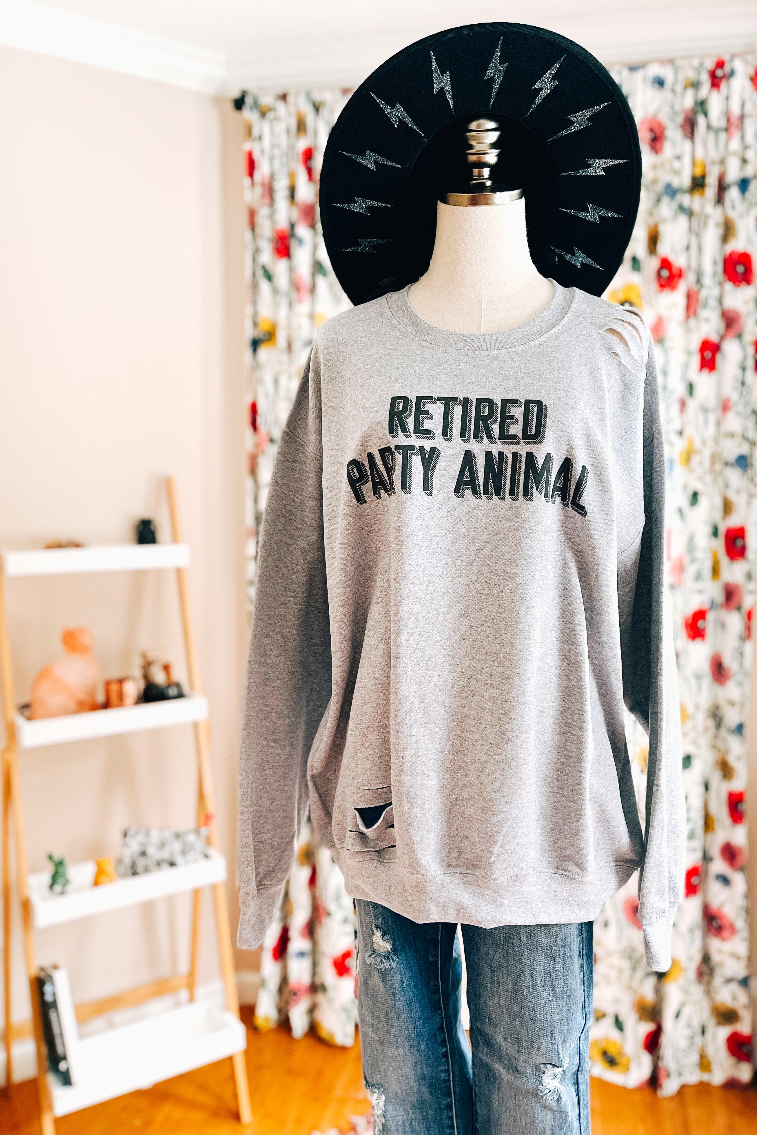 Grey distressed pullover featuring "Retired Party Animal" text styled on mannequin with black hat indoors
