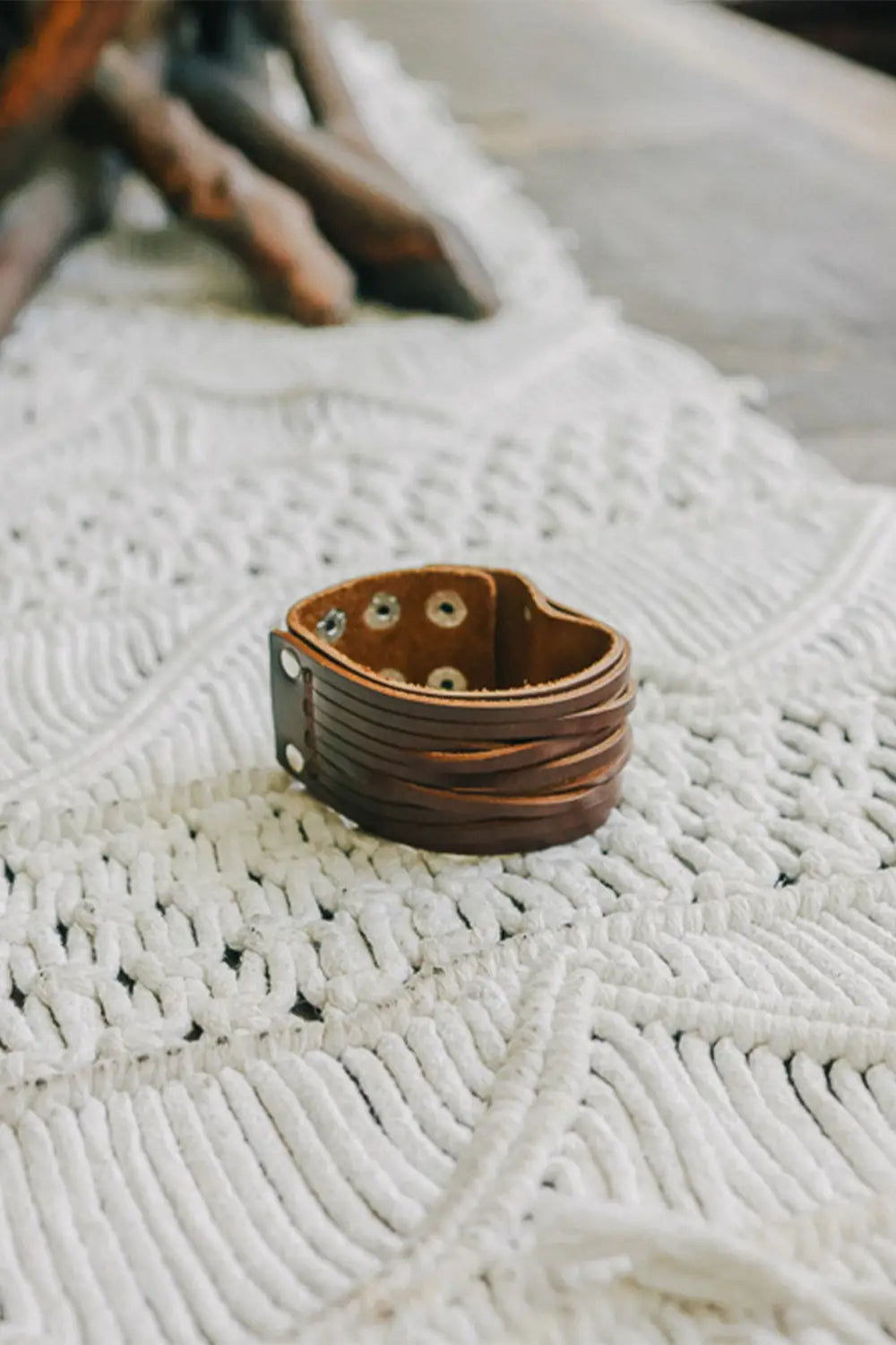 Brown leather cuff bracelet with metal snap closures resting on textured white fabric surface