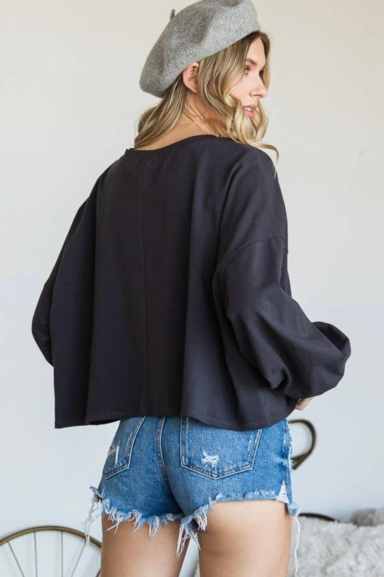 Woman wearing charcoal oversized long sleeve crop top and frayed denim shorts with grey beret against white wall