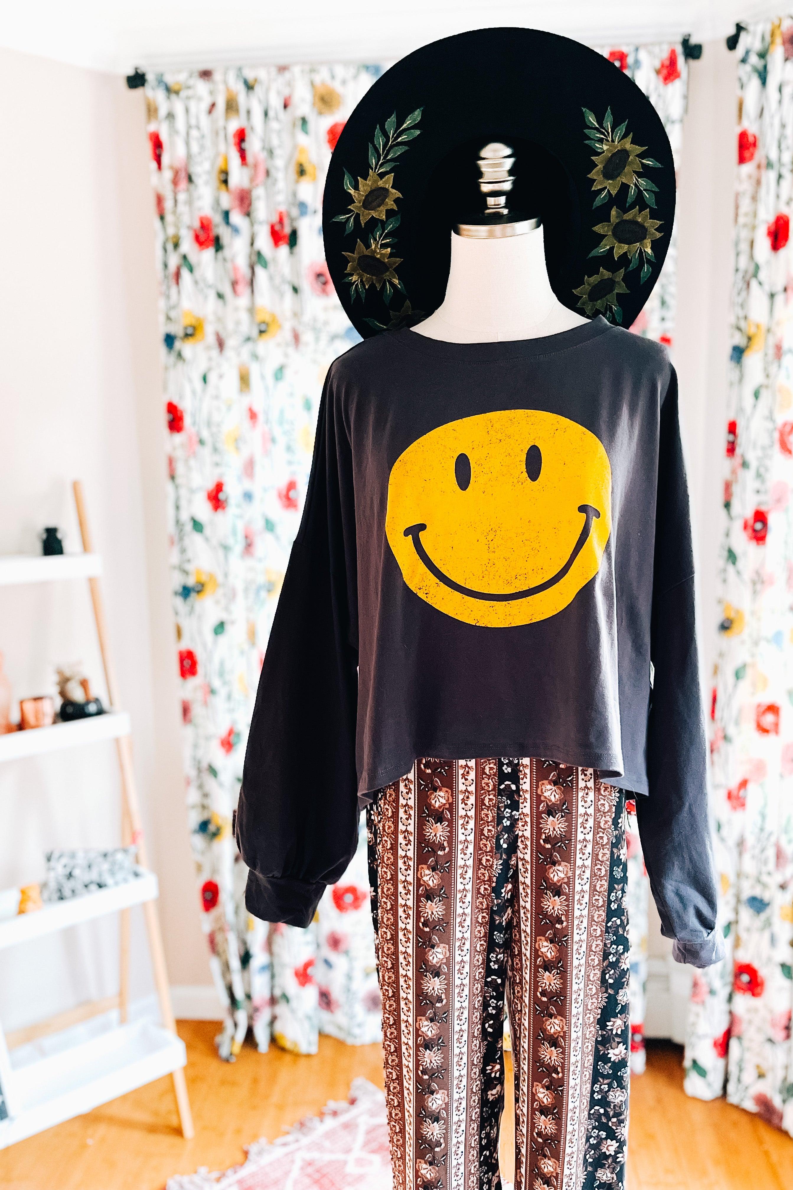Charcoal long sleeve crop top with yellow smiley face paired with patterned boho-style pants on mannequin indoors