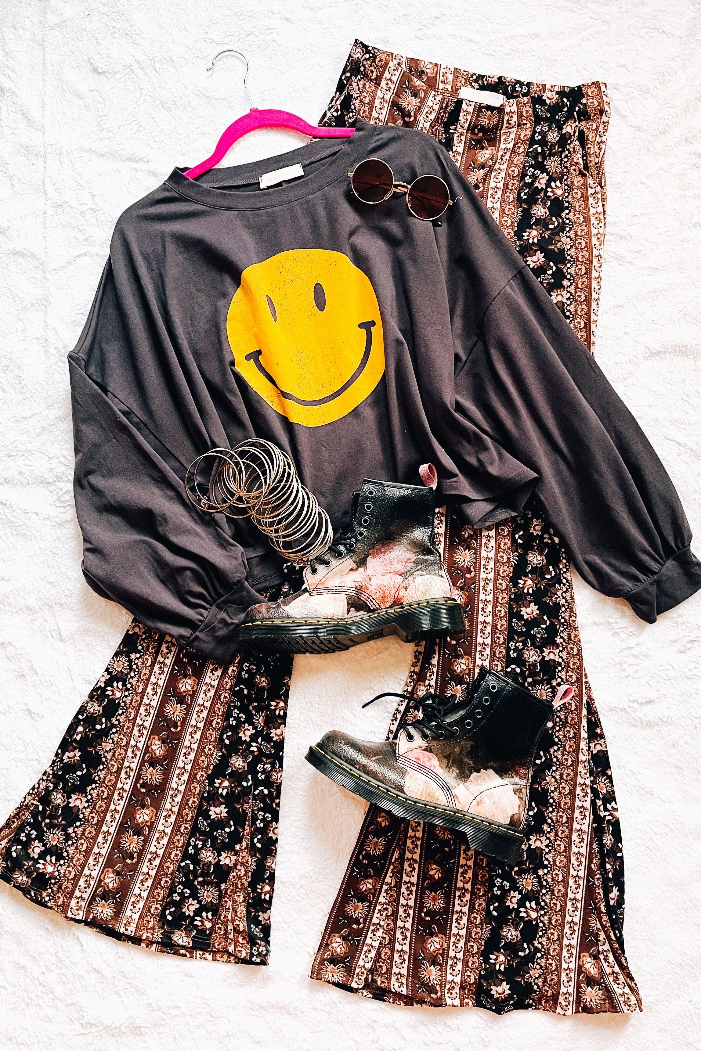 Charcoal long sleeve crop top with large yellow smiley face paired with floral patterned wide-leg pants and lace-up boots