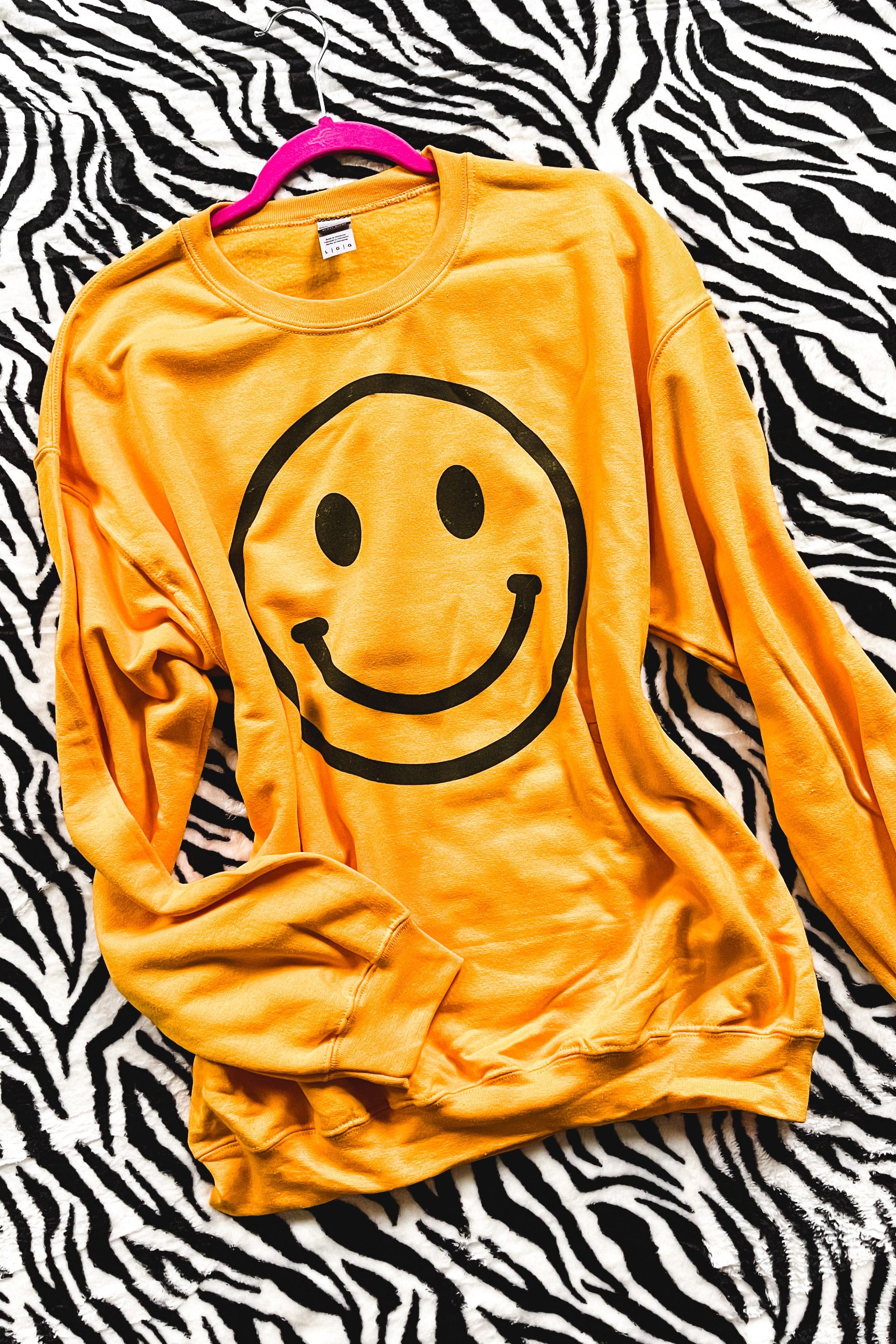 Yellow sweatshirt featuring a large black smiley face graphic laid over zebra print fabric on pink hanger