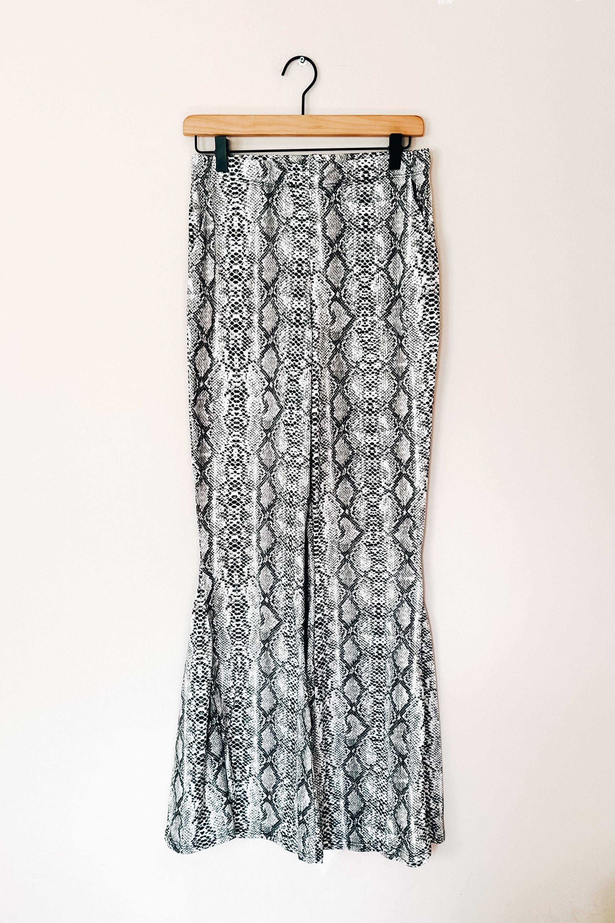 Grey snake print flare pants hanging on wooden hanger against plain background