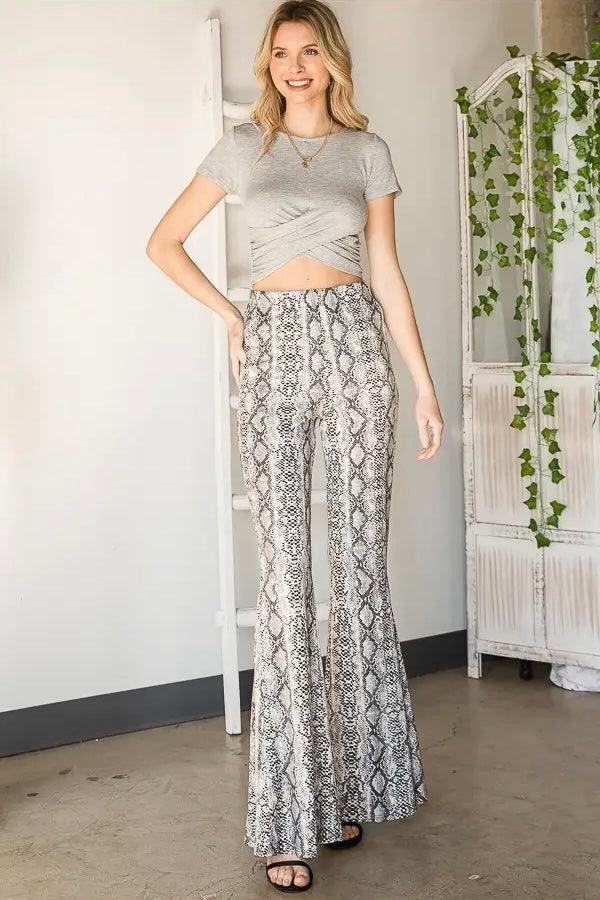 Smiling woman wearing grey cropped wrap top with high-waisted grey snake print flare pants and black sandals indoors