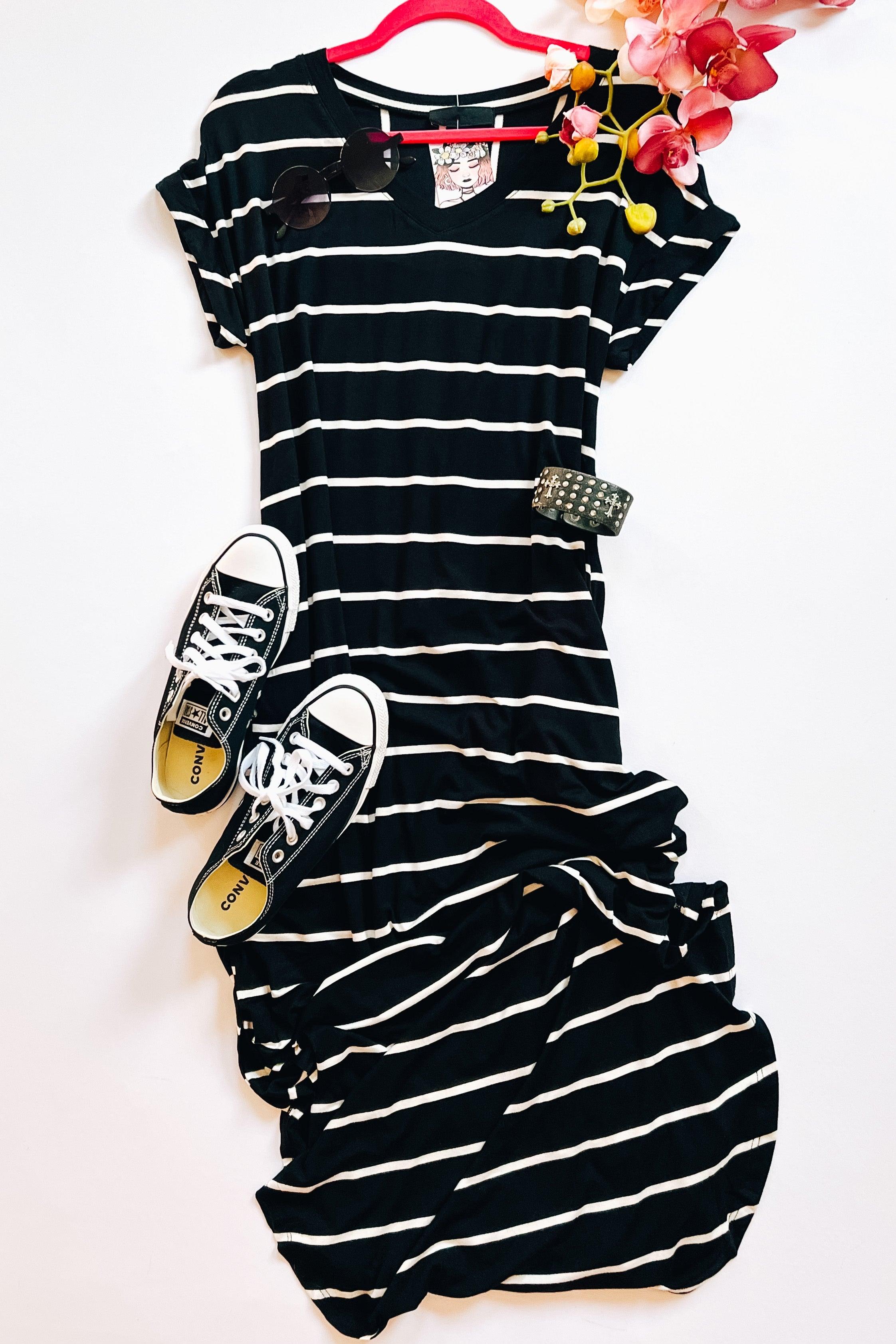Black and white striped maxi dress styled with black Converse sneakers, sunglasses, floral accent, and studded bracelet on white background