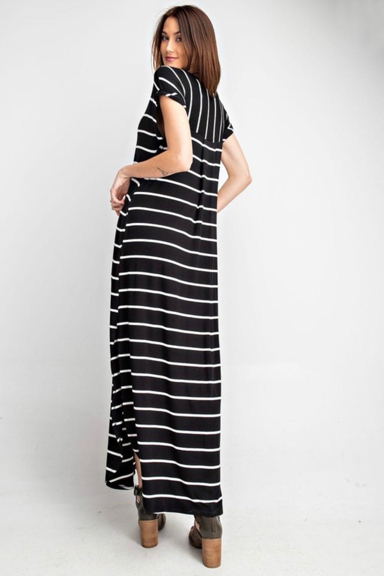 Woman wearing a black maxi dress with white stripes, posing with hands on hips and looking over shoulder