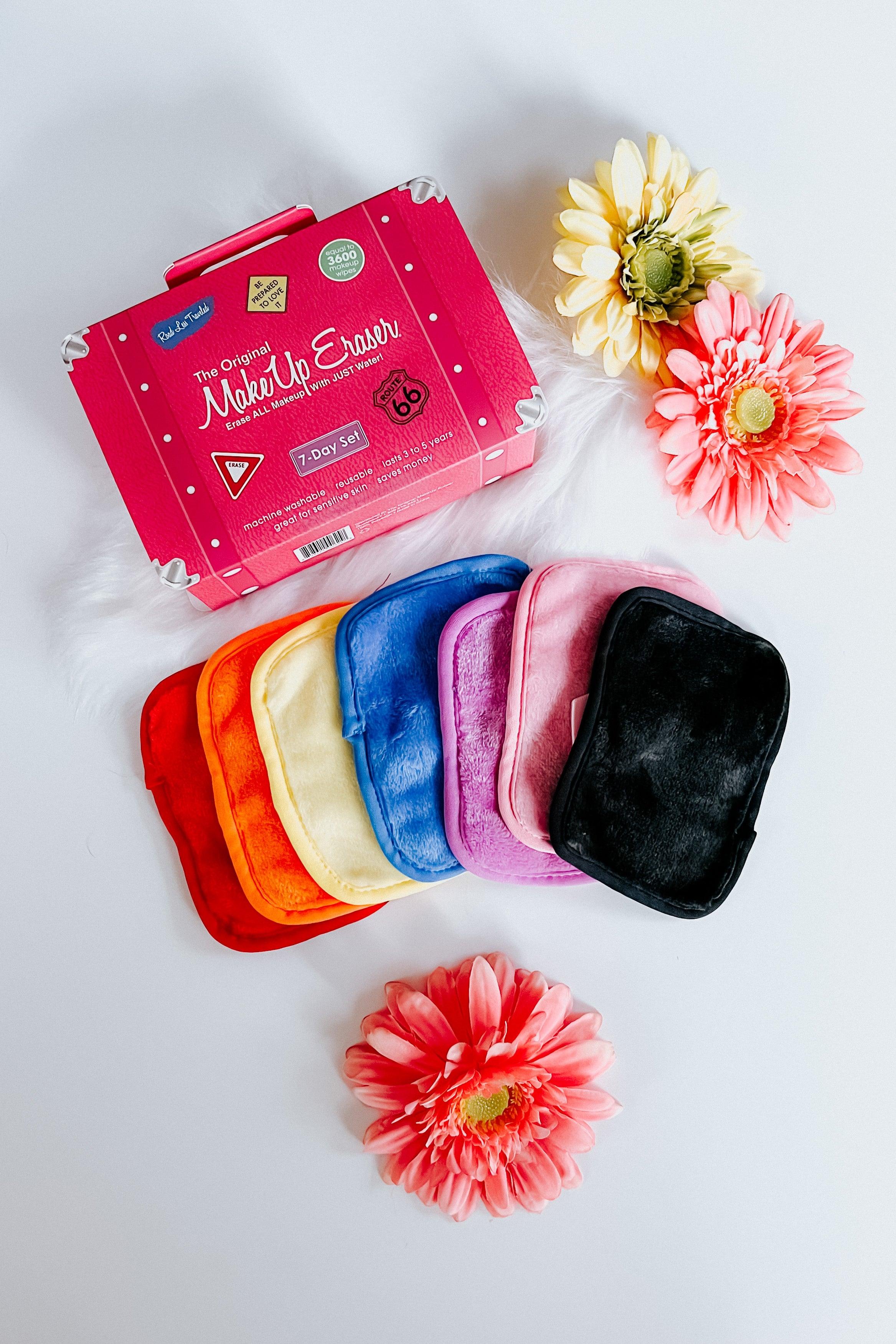 Rainbow-colored reusable makeup remover cloths arranged in a fan beside a pink branded box and fresh flowers on white background