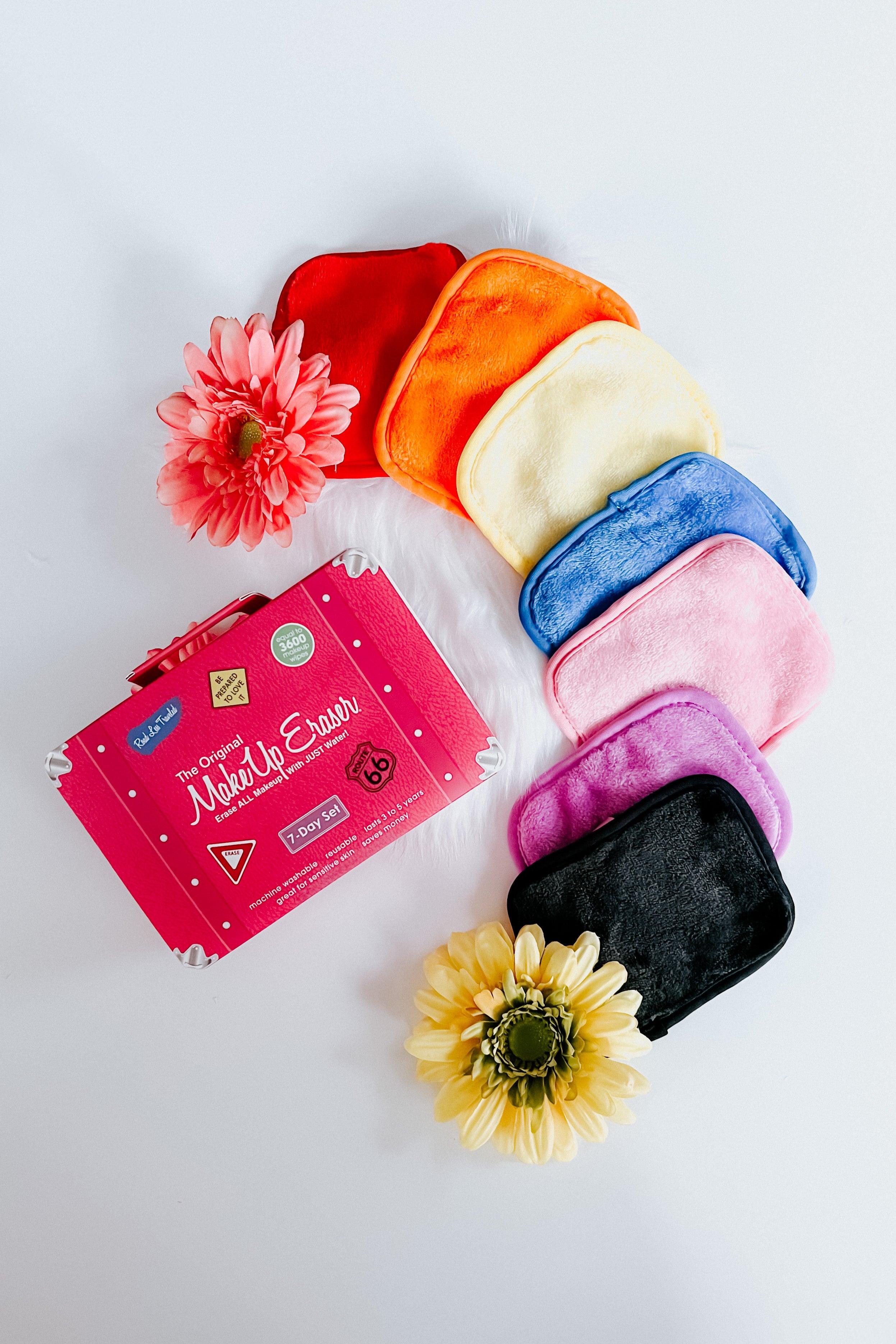 Bright reusable makeup remover cloths in rainbow colors arranged beside pink branded case and artificial flowers