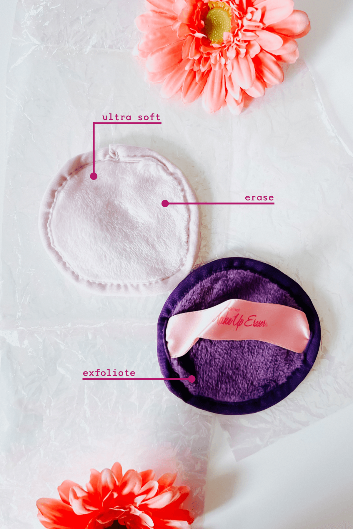 Two round reusable makeup remover pads in pink and purple labeled ultra soft, erase, and exfoliate with pink flowers nearby