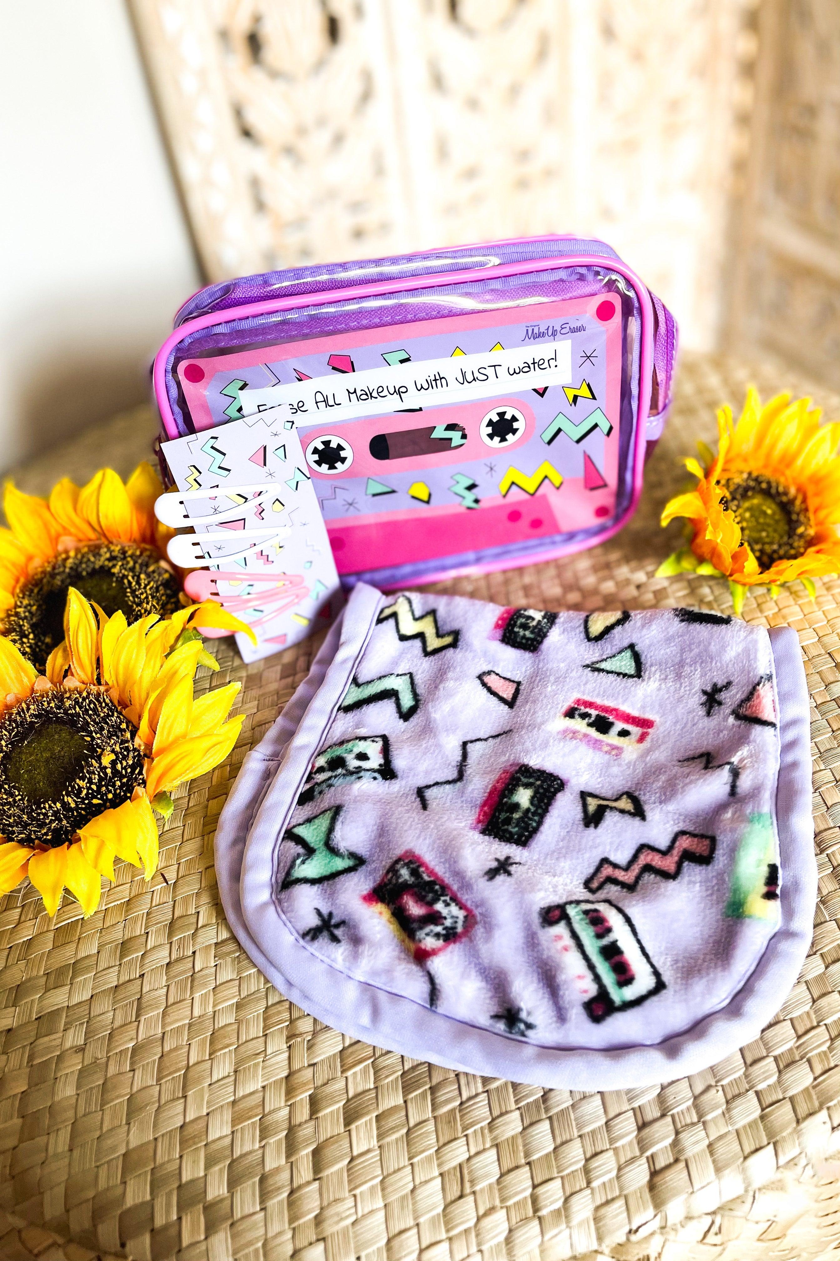 Purple plush makeup remover cloth with retro cassette design beside clear purple zippered pouch and sunflowers