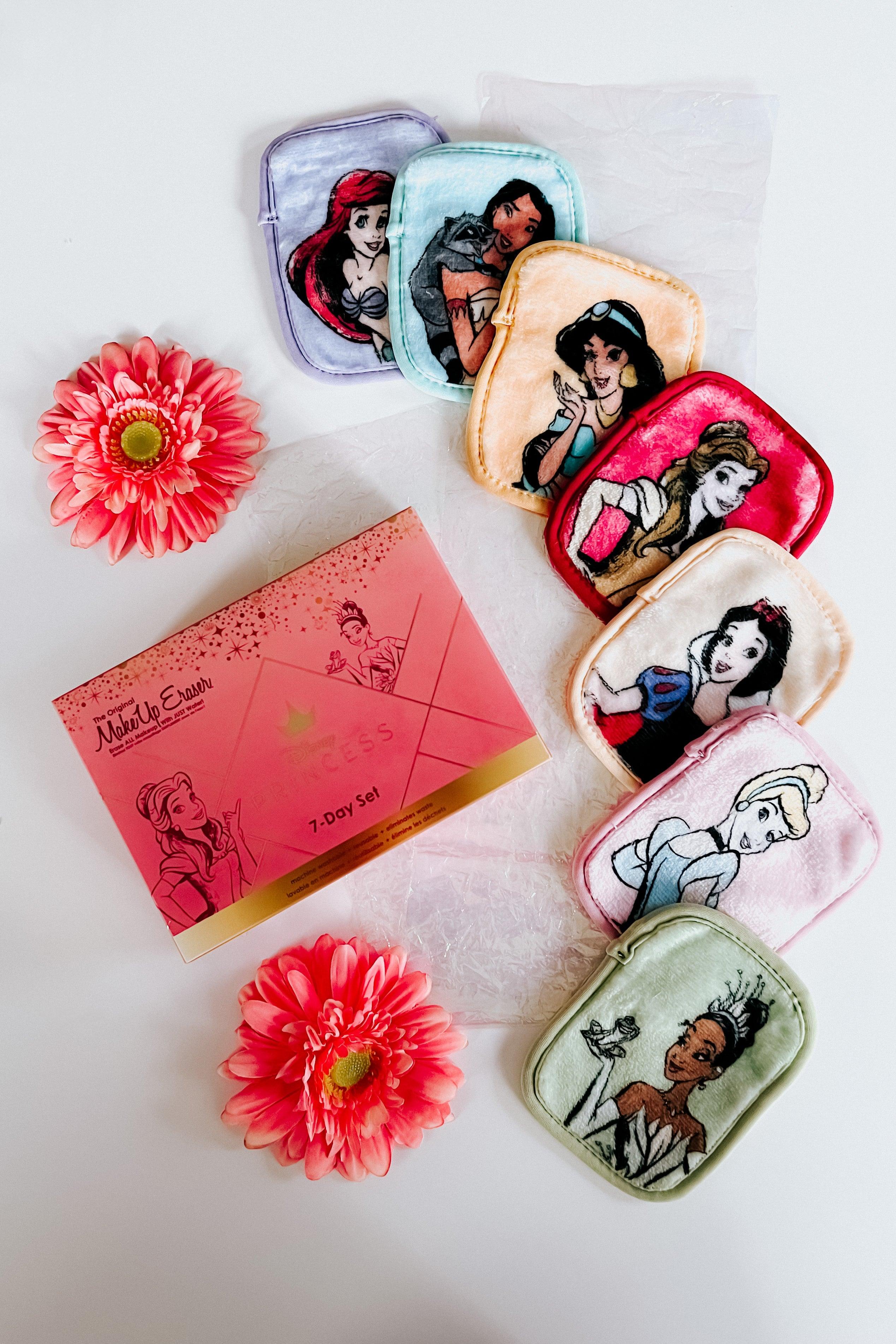 Multicolor Disney princess-themed makeup eraser pads arranged next to pink flowers and a pink box on white surface