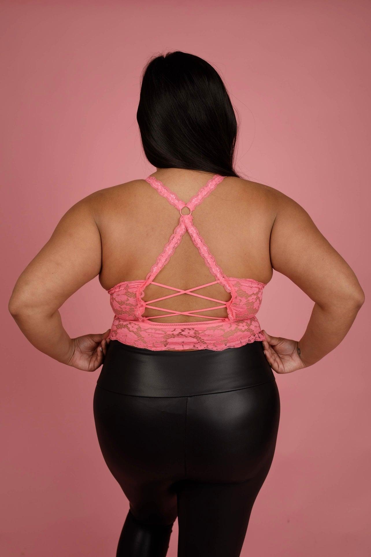 Plus-size woman seen from the back wearing a pink lace bralette with crisscross straps and black faux leather pants