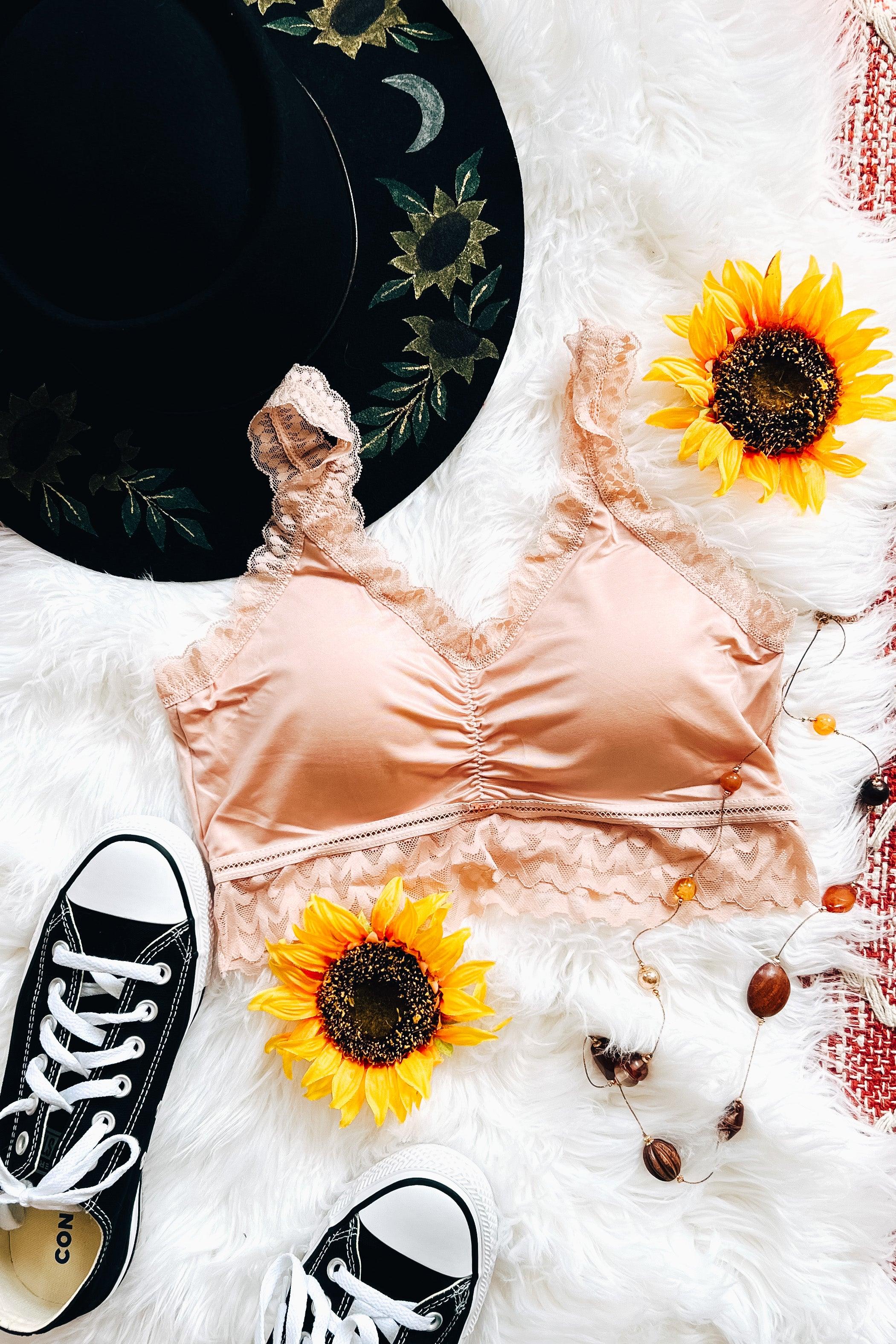 Soft pink bralette with lace trim styled with black embroidered hat, sneakers, sunflowers, and rustic beads on white fur background