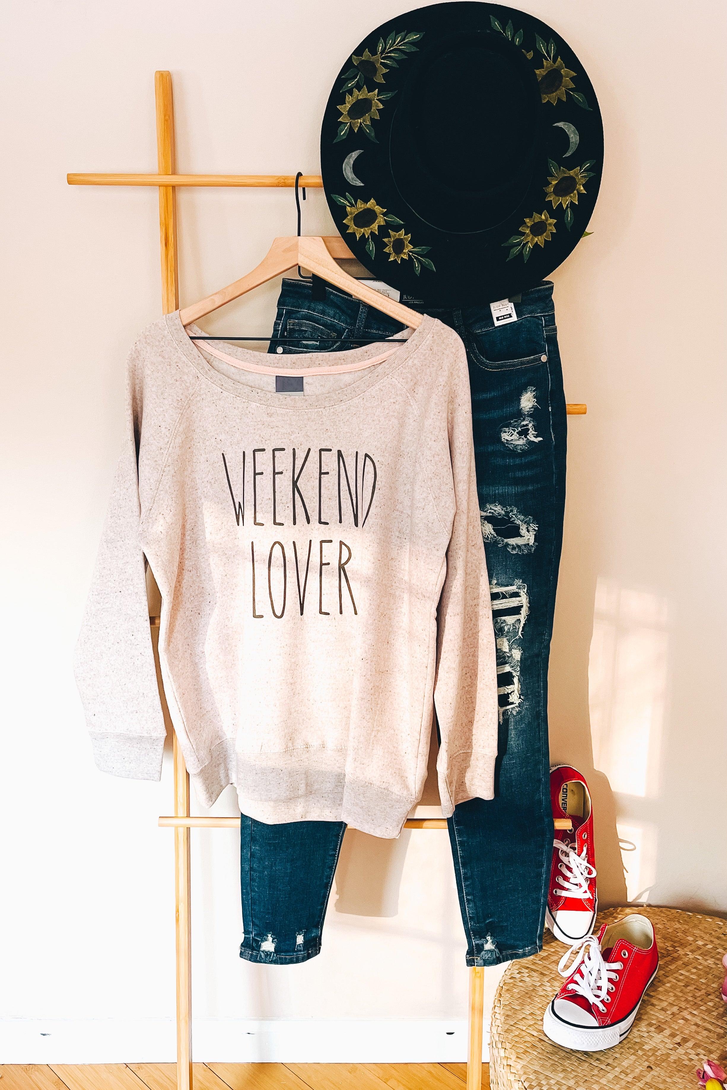 Blush scoop neck pullover with "Weekend Lover" text paired with distressed jeans and embroidered black hat indoors
