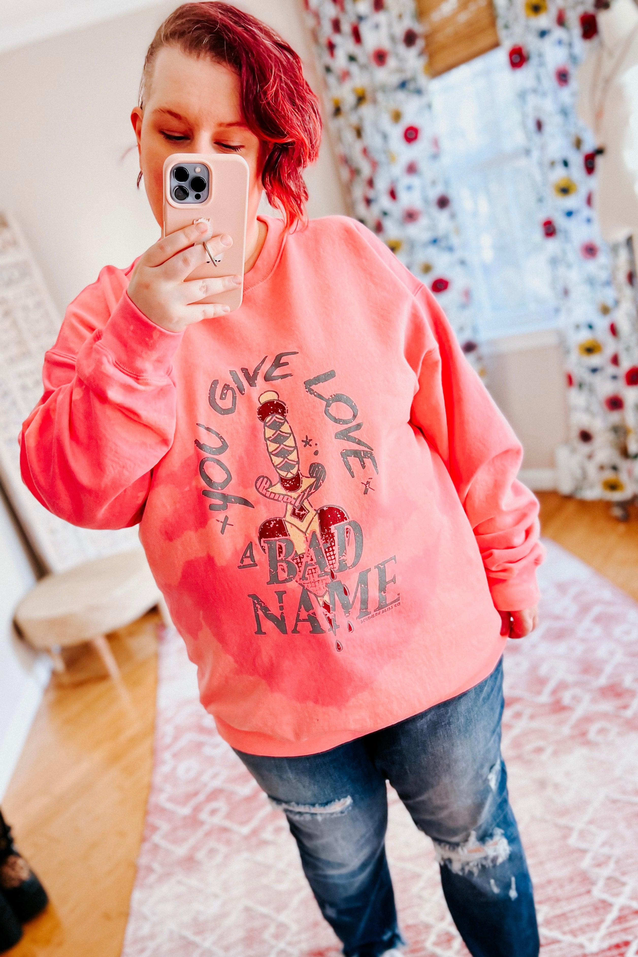 Woman with short red hair wearing a pink bleached pullover with graphic text and distressed blue jeans indoors