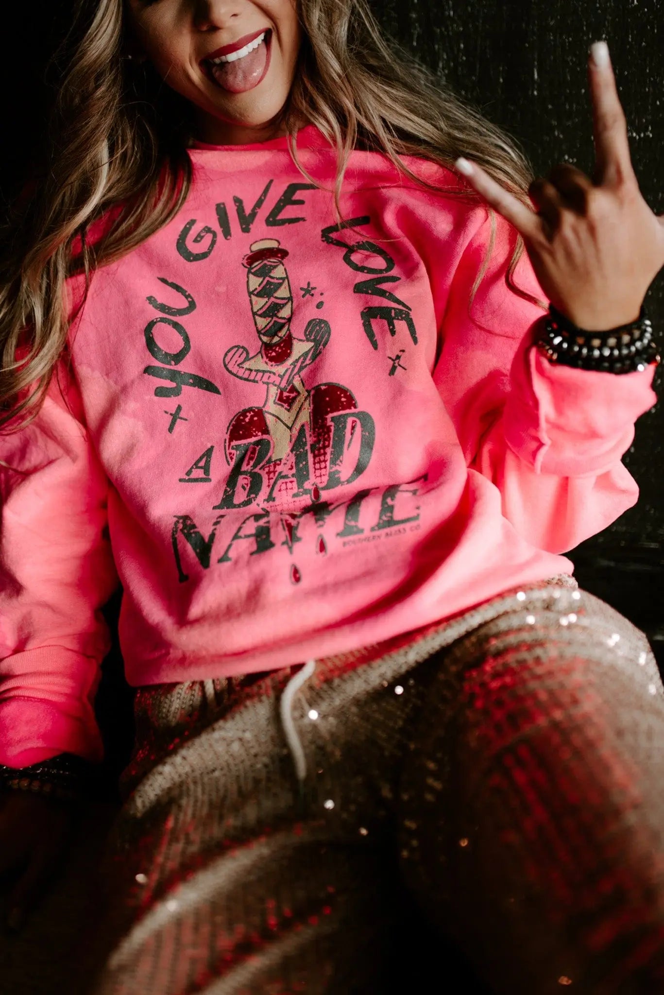 Woman wearing bright pink bleached pullover with bold graphic text and sequined pants in casual pose
