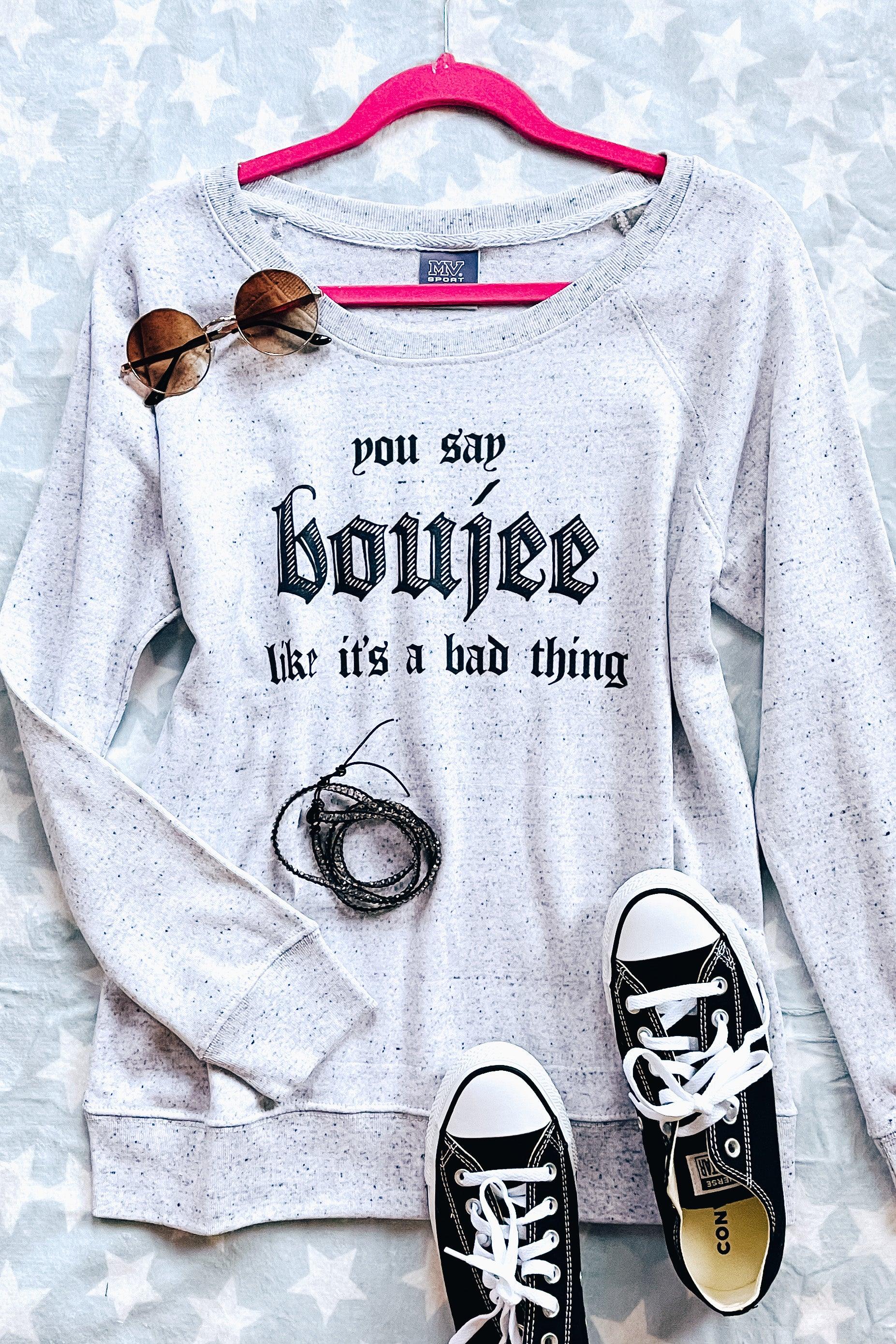 Light grey speckled pullover with bold lettering styled with round sunglasses, black sneakers, and a bracelet on star-patterned background