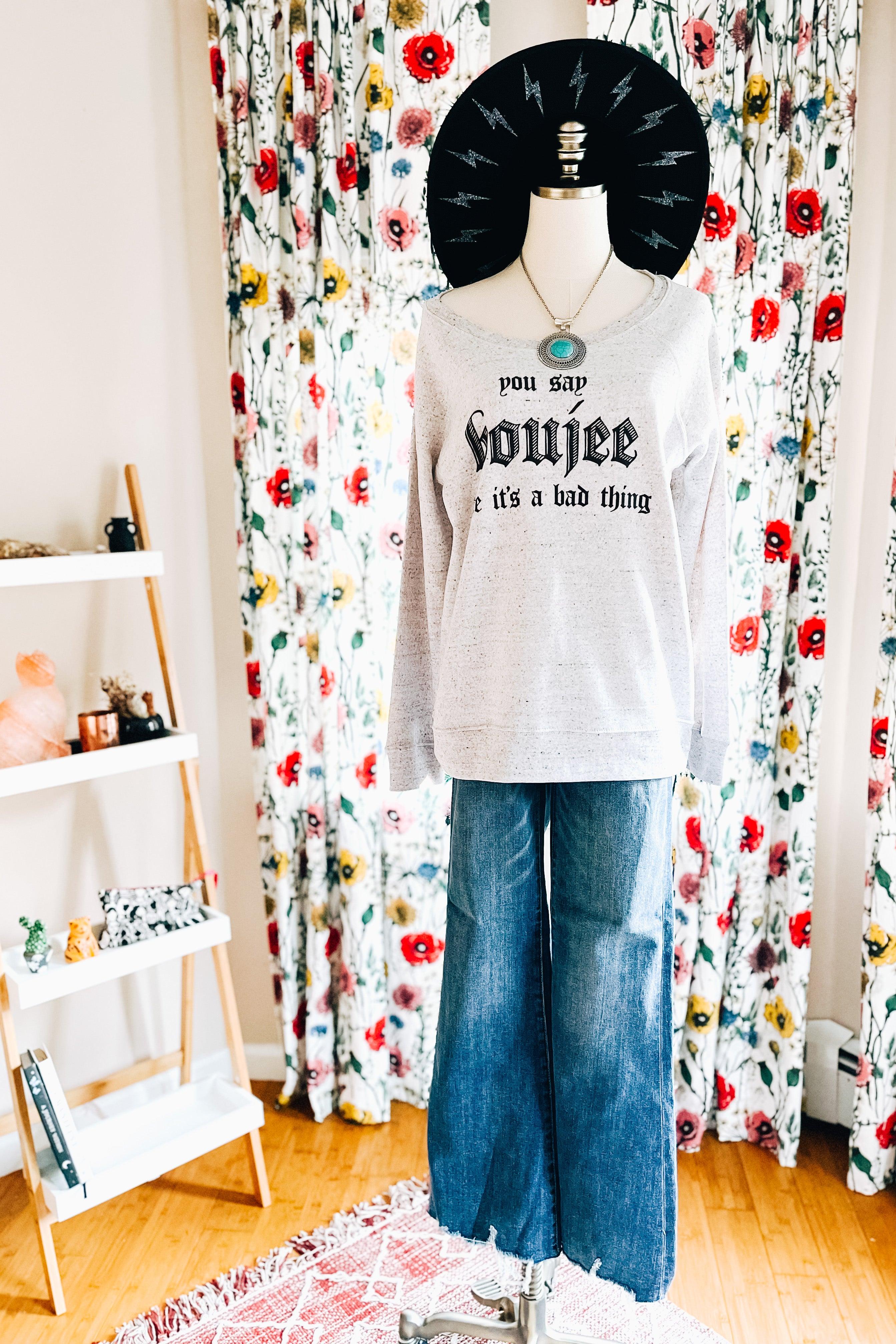 Grey speckled pullover with bold text styled with wide-leg jeans and layered necklace on mannequin indoors