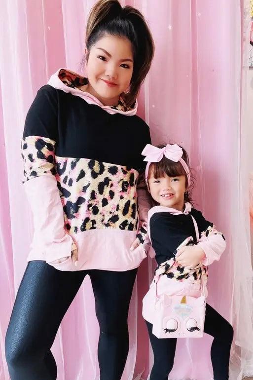 Woman and girl wearing black and pink hoodies with leopard print and black leggings in front of pink backdrop