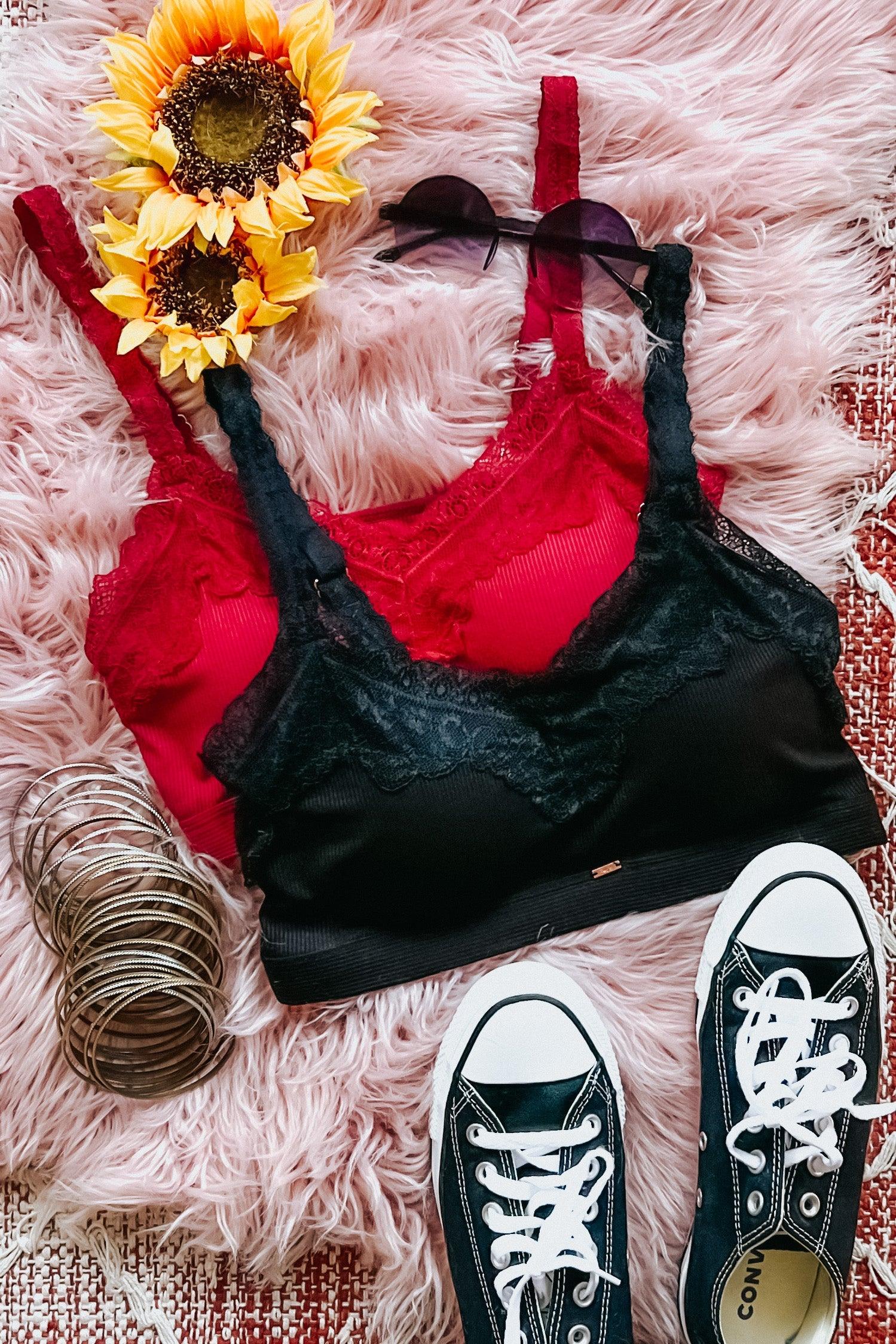 Black lace trim bralette layered over red one with sunglasses, sunflowers, bracelets, and black sneakers on pink fur rug