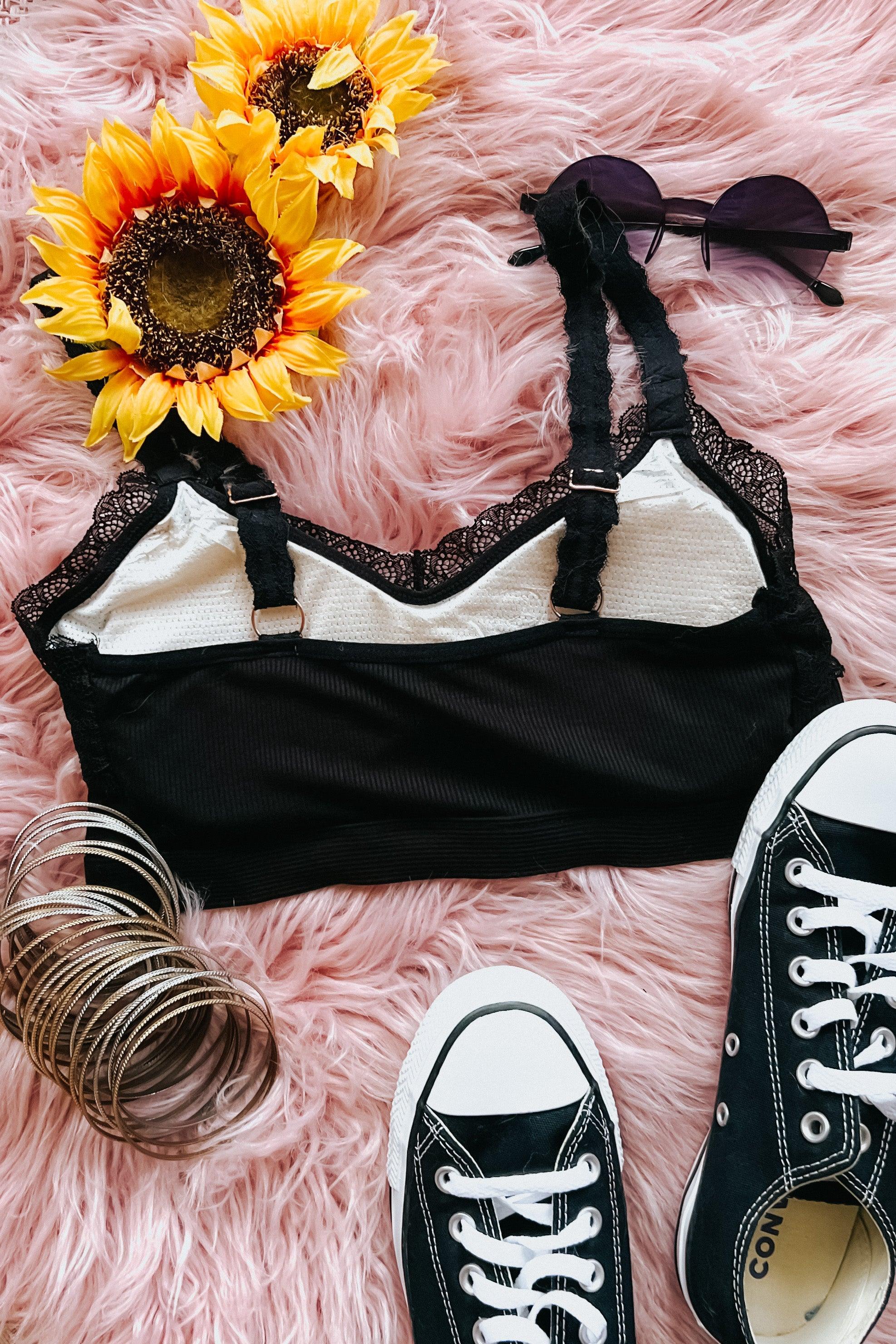 Black lace-trim bralette styled with round sunglasses, sunflower accents, silver bangles, and classic black sneakers on pink fur
