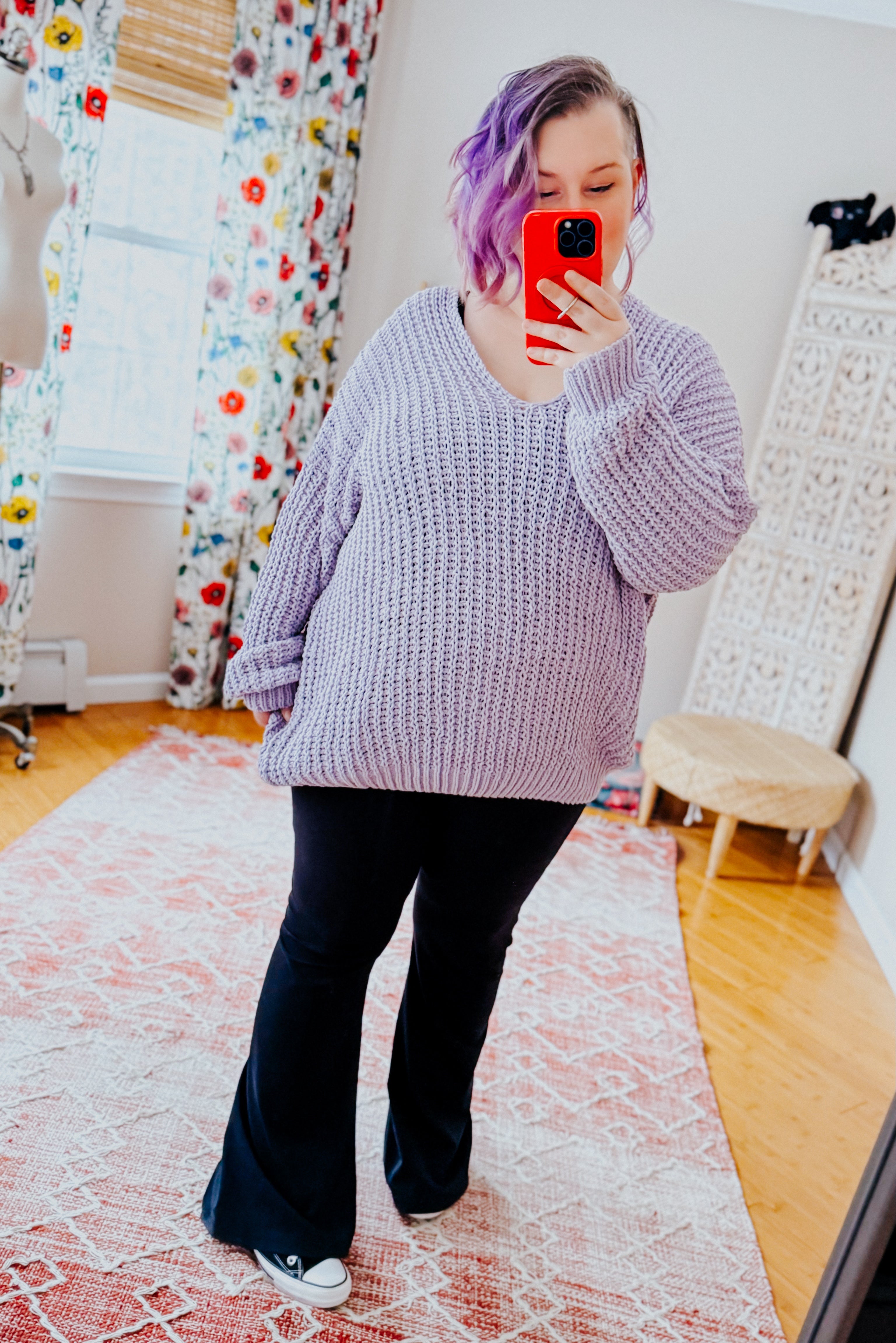 Woman wearing a chunky lavender sweater and black yoga pants in an indoor setting.