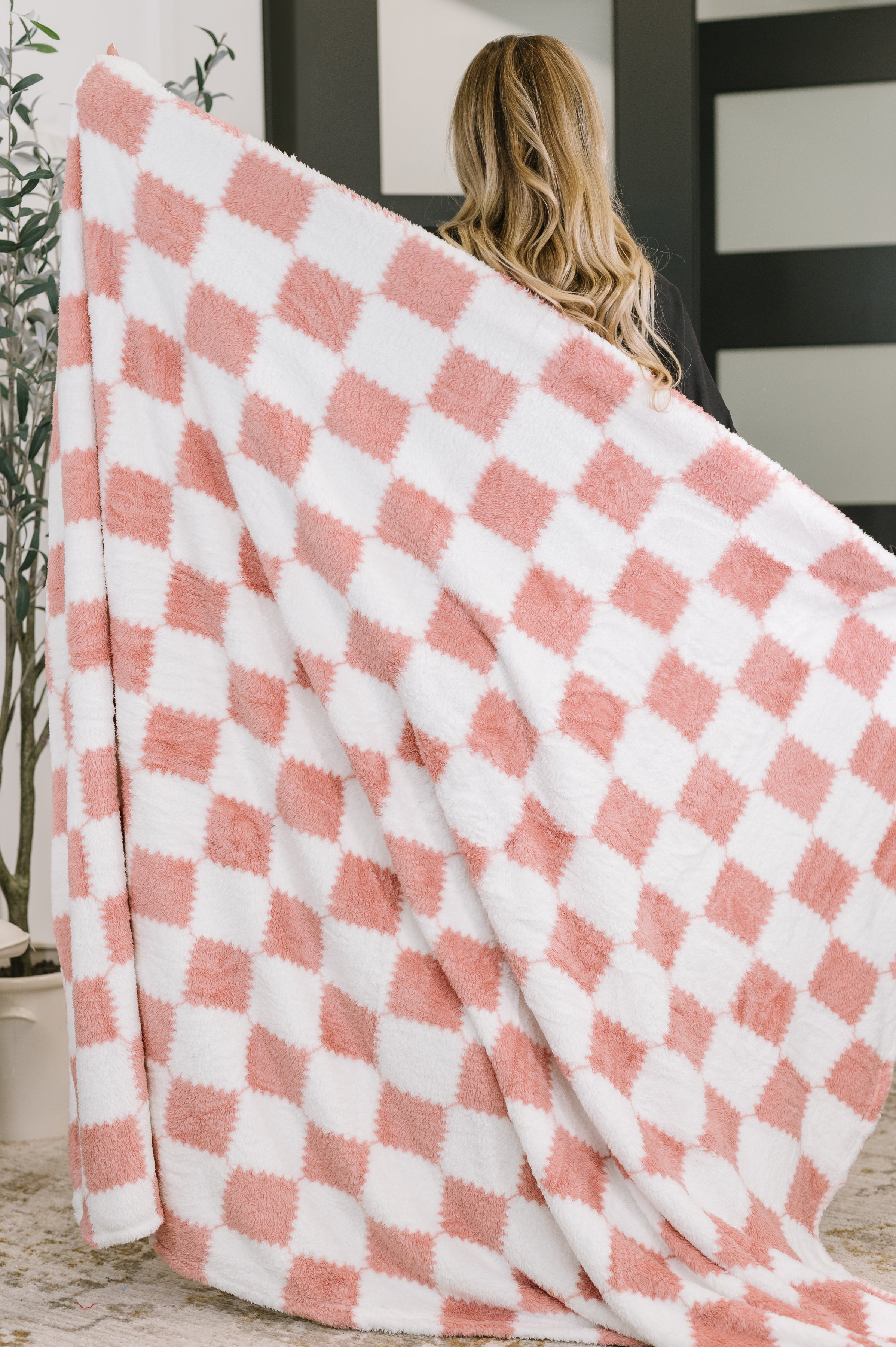 Woman holding a pink and white checkered blanket indoors.