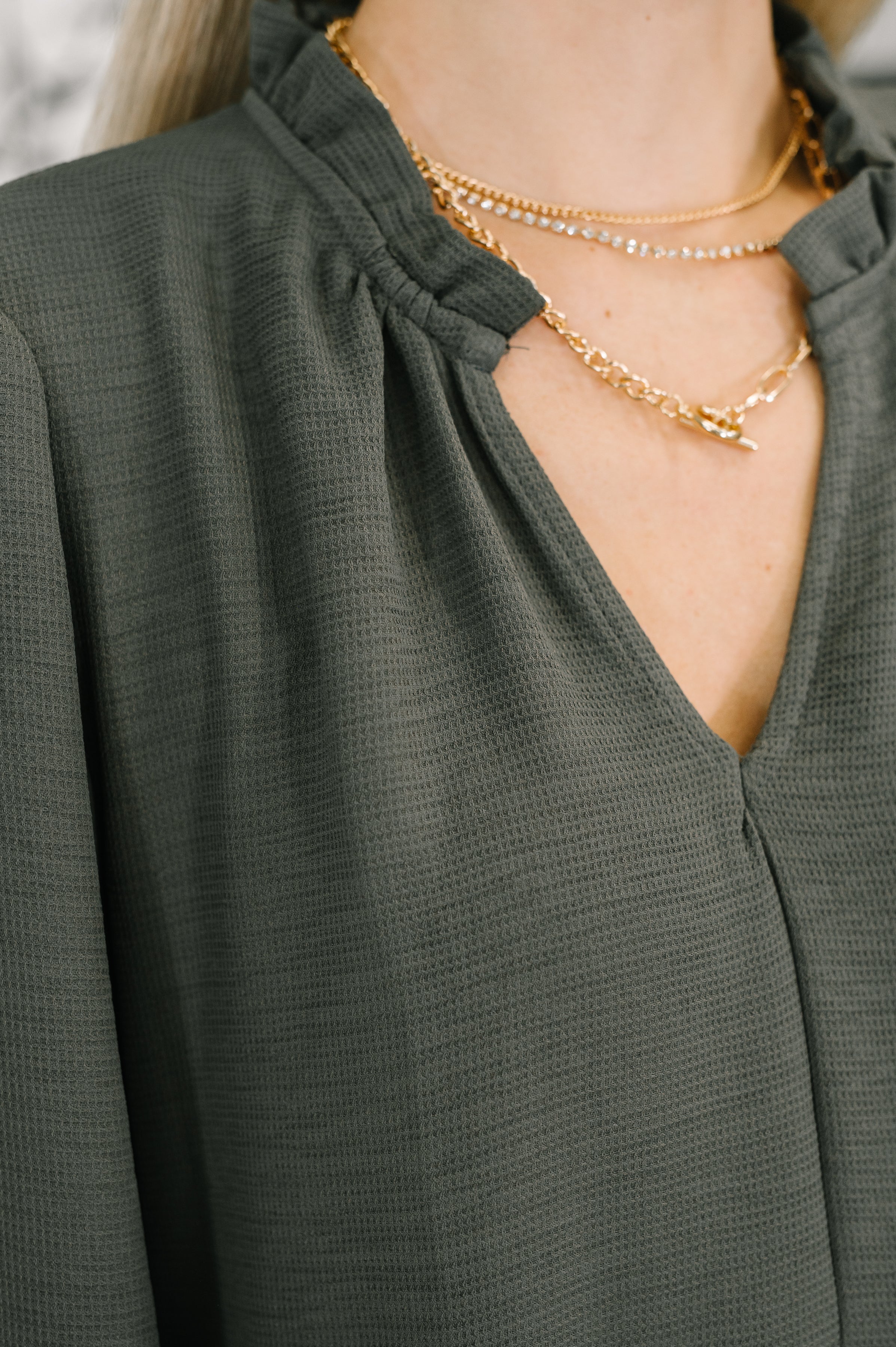 A close up of a grey dress with a deep neckline and a gold necklace.