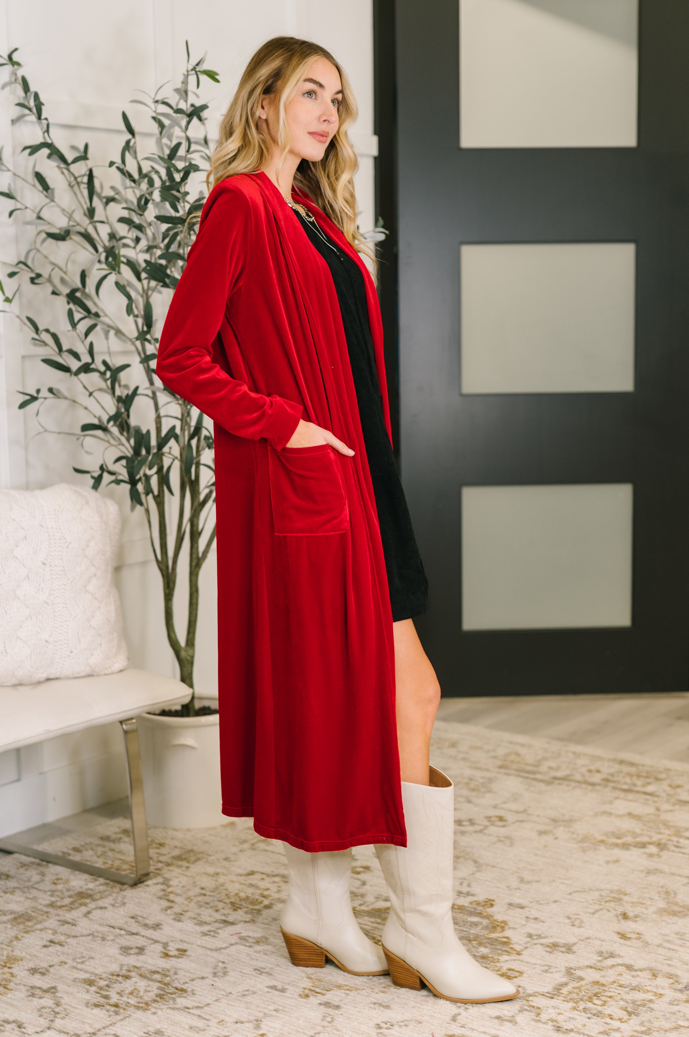 Woman wearing a red cardigan over a black dress with white boots in an indoor setting.