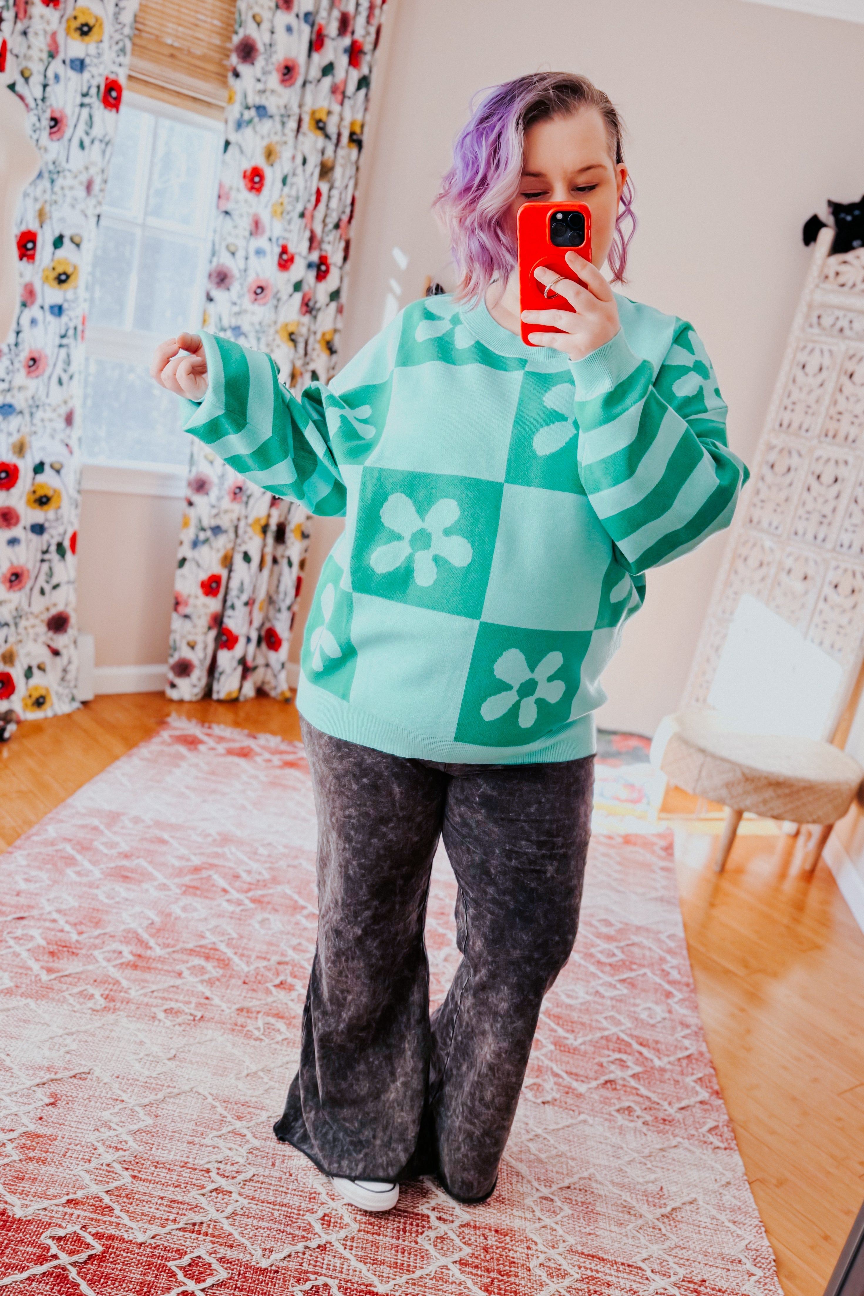Woman wearing a checkered floral print mint sweater over acid wash flared pants in an indoor setting.