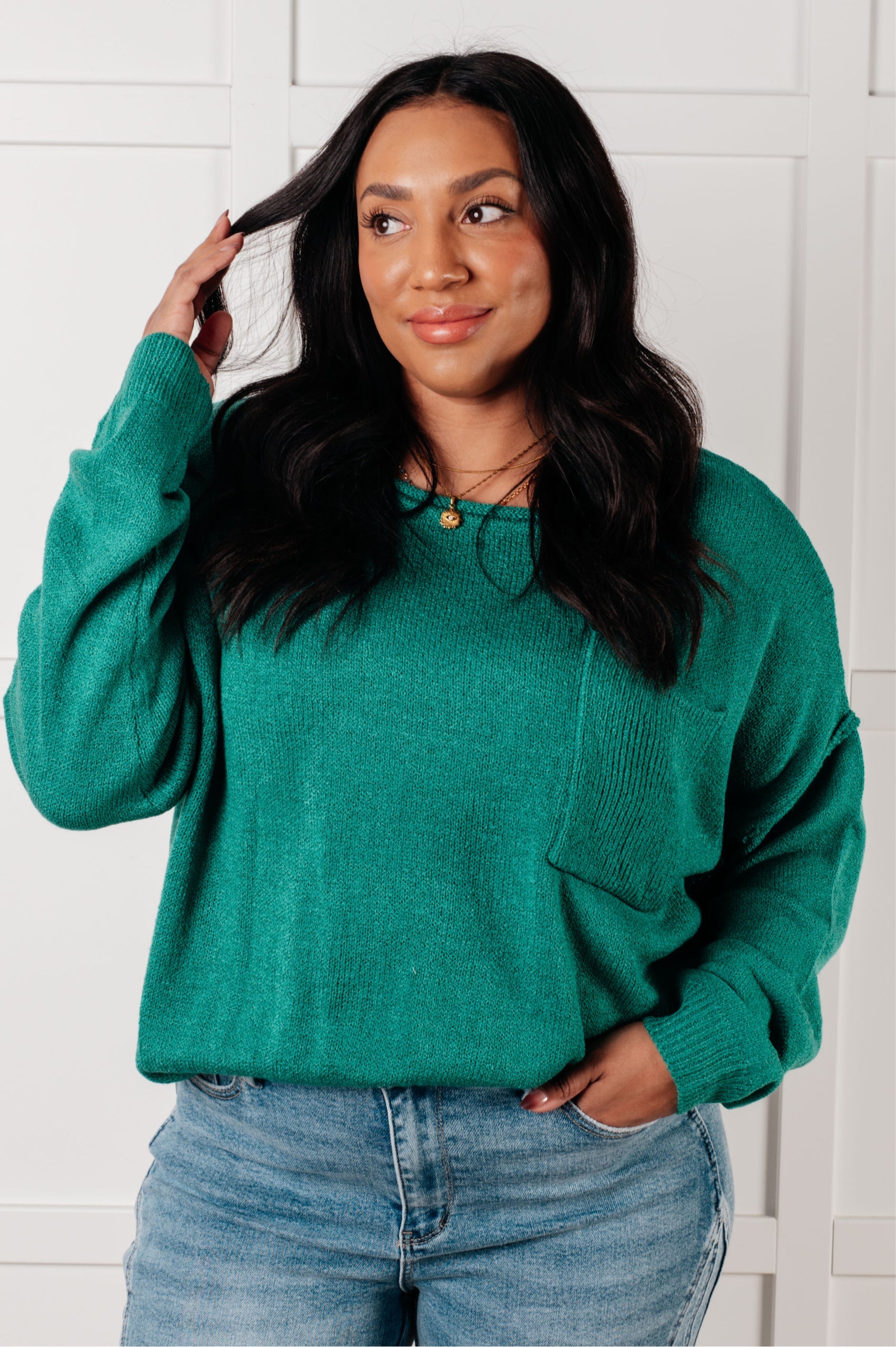 Woman wearing a teal sweater and blue jeans against a white wall.