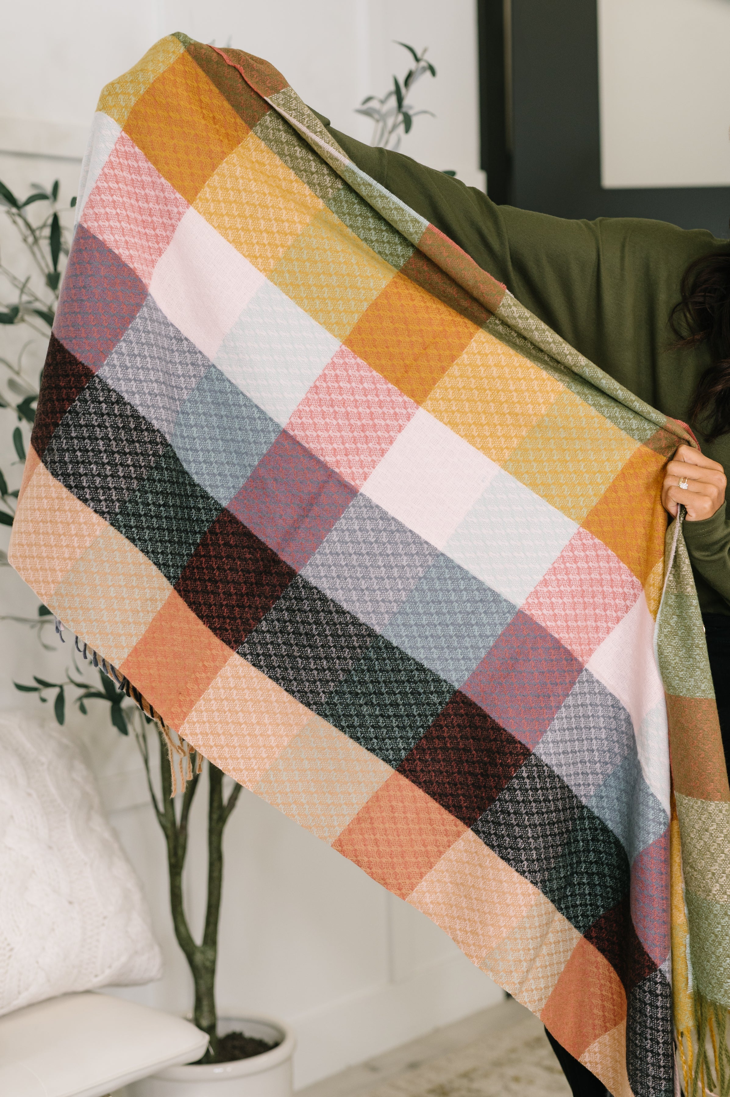 Woman holding a colorful checkered scarf with fringe in a home setting
