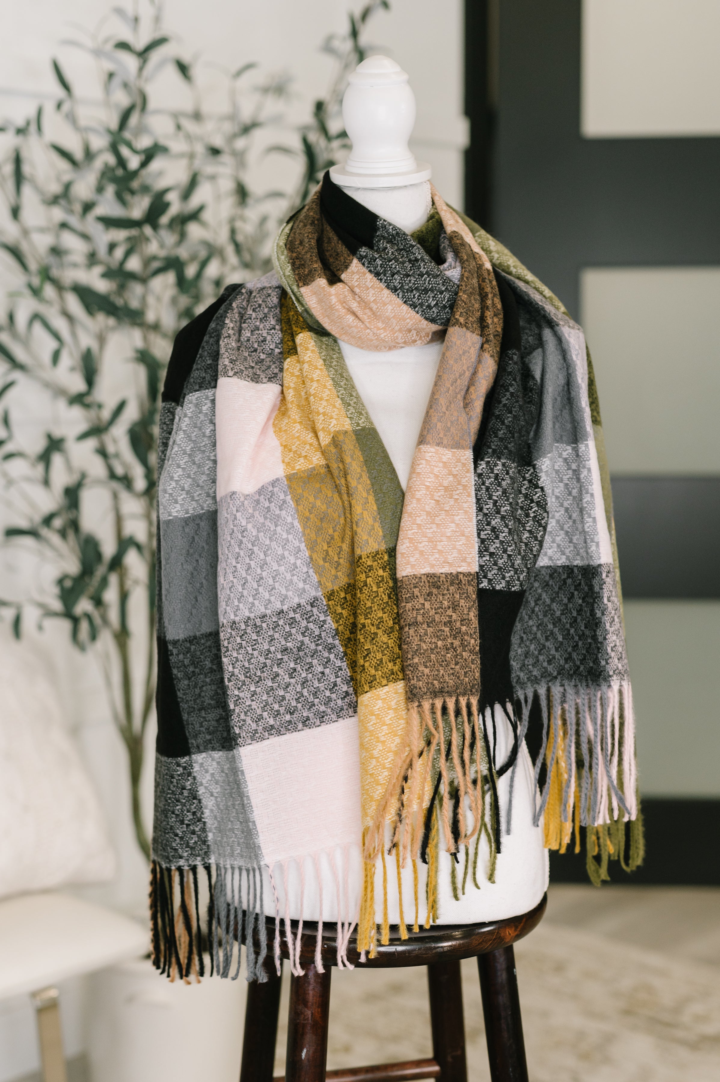 A colorful checkered scarf with fringe draped over a dress form in an indoor setting.