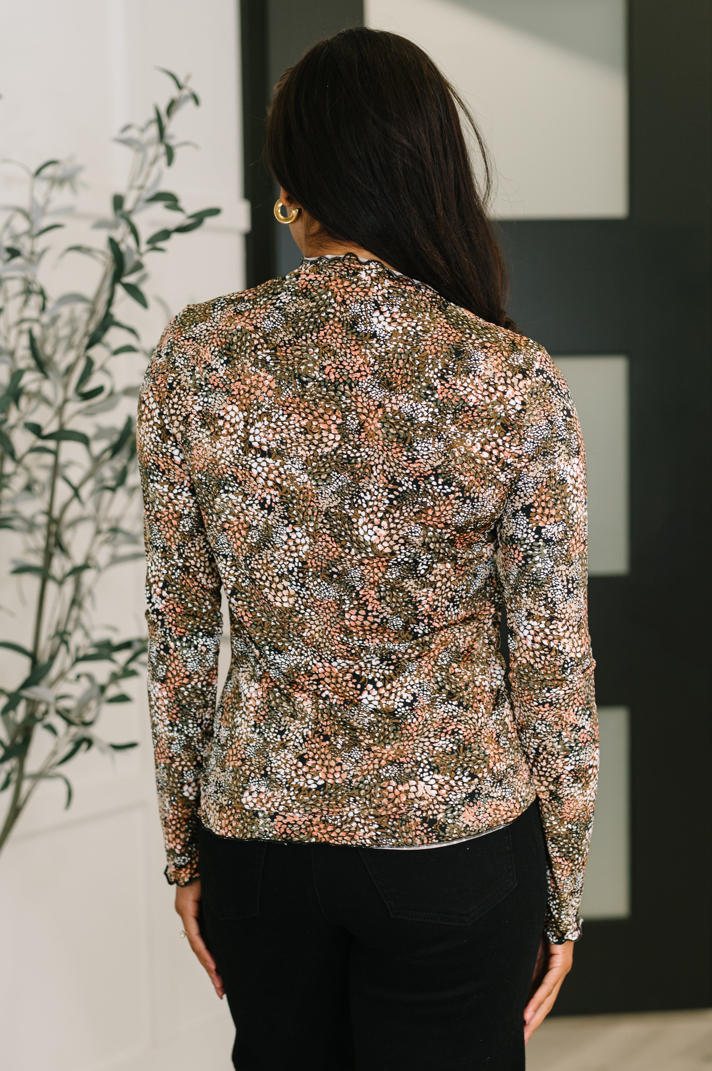 Woman wearing a floral green and orange long-sleeve top and black pants in an indoor setting.