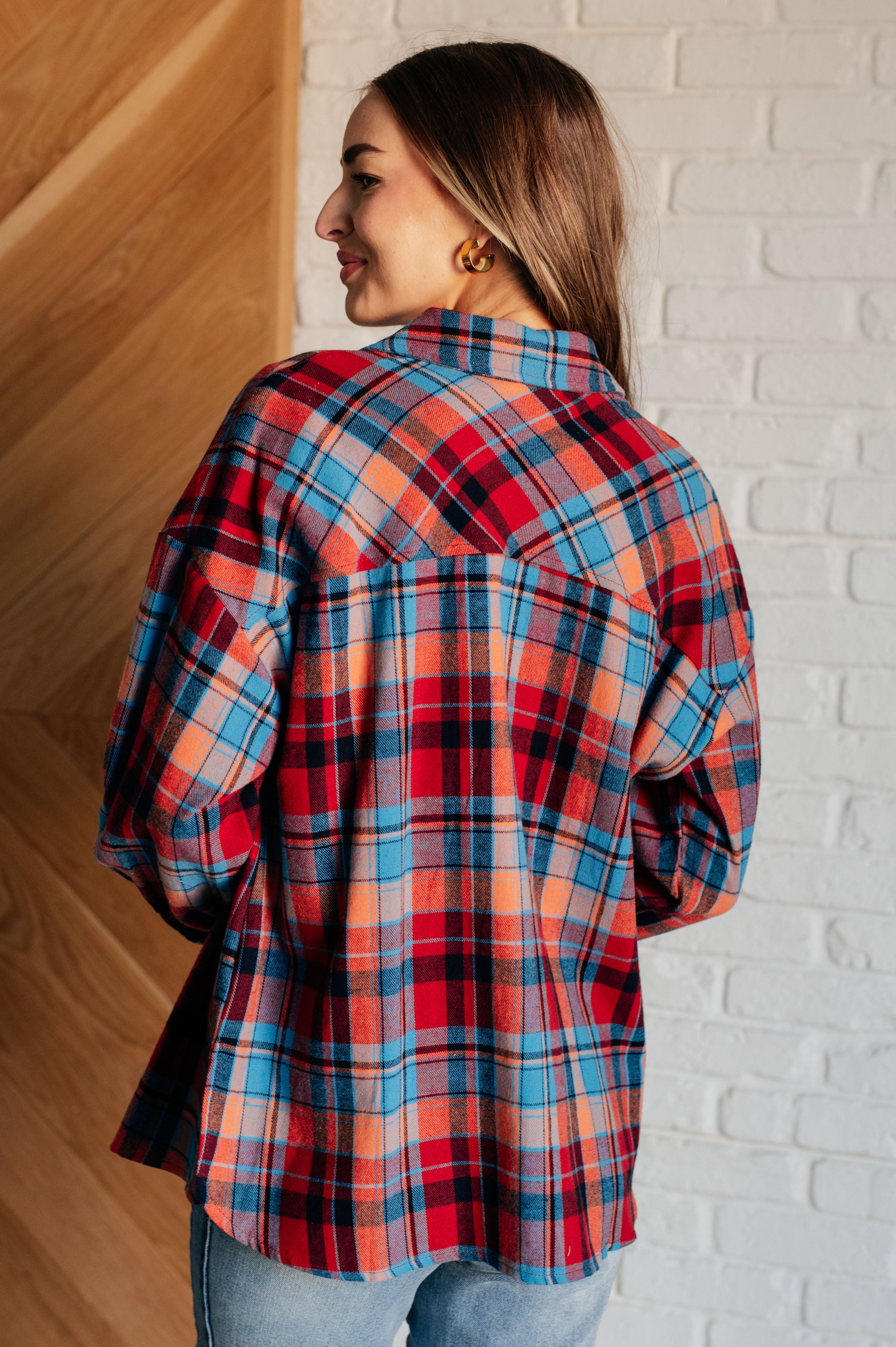 Woman wearing a red and blue long-sleeves plaid button-up shirt blue jeans with a white brick wall background.