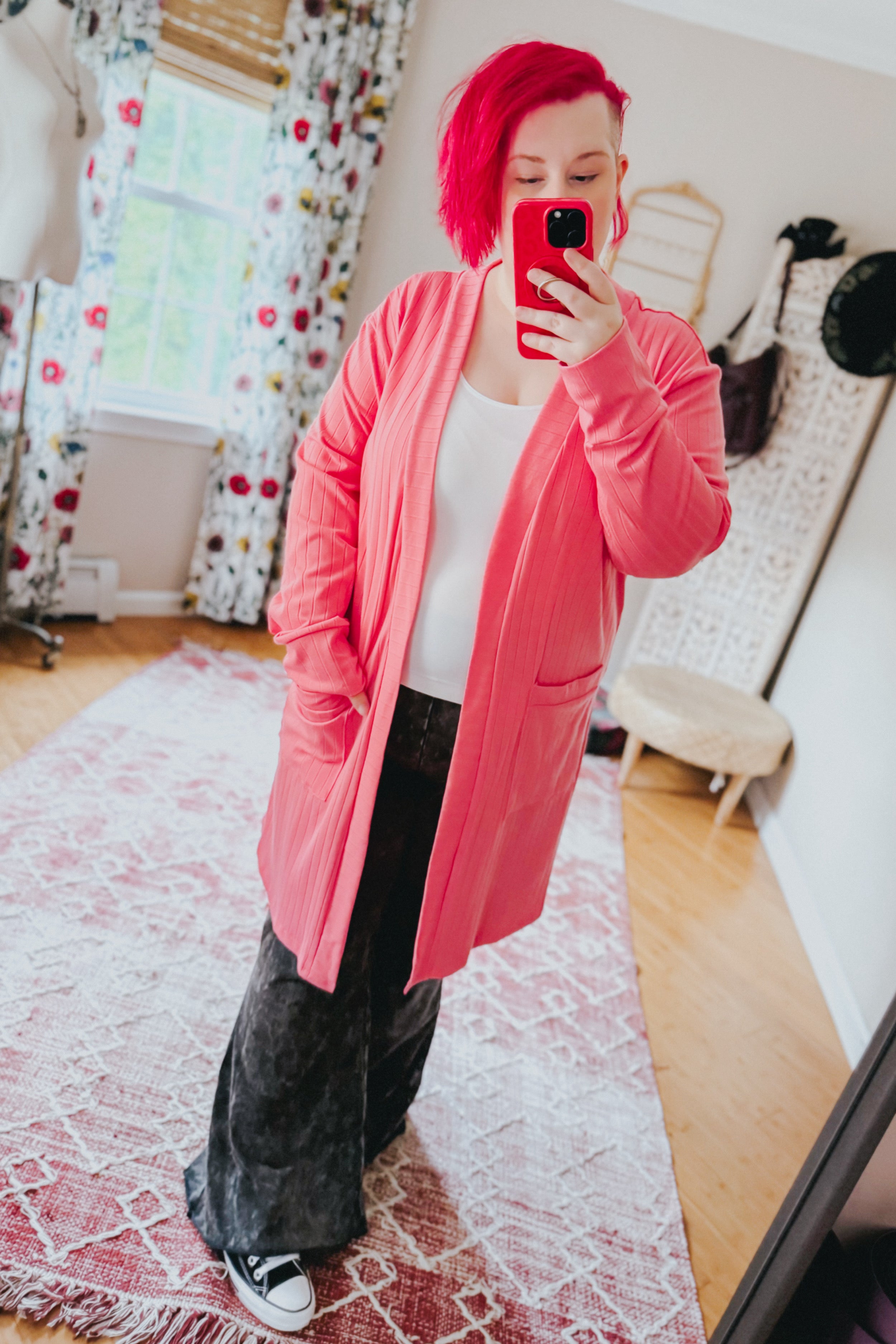 Woman taking mirror selfie wearing coral Modern Idealist open front cardigan with pockets over white top and wide dark pants indoors