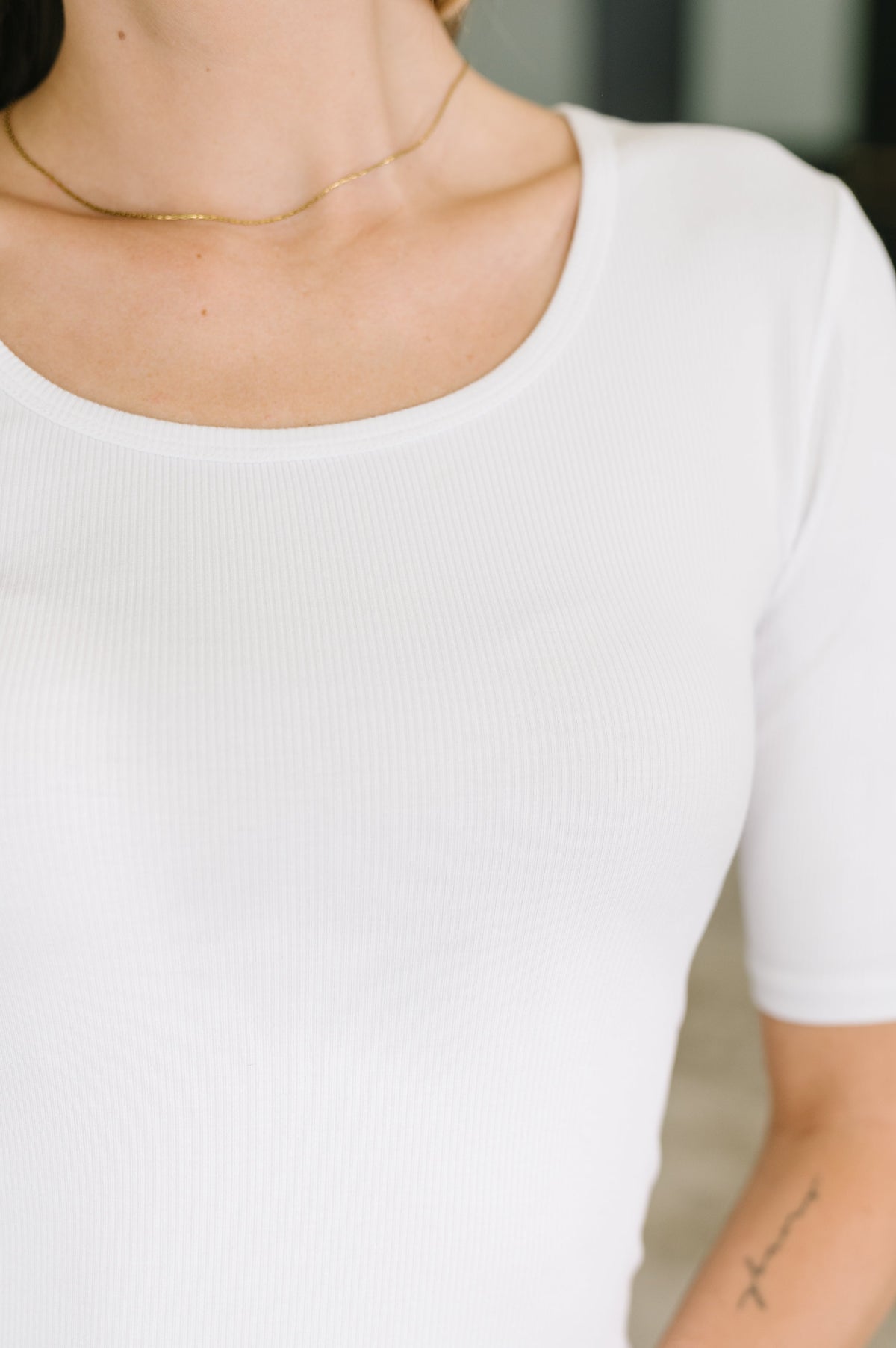 Close view of a woman wearing a fitted white ribbed knit U neck top with half sleeves and a delicate gold necklace