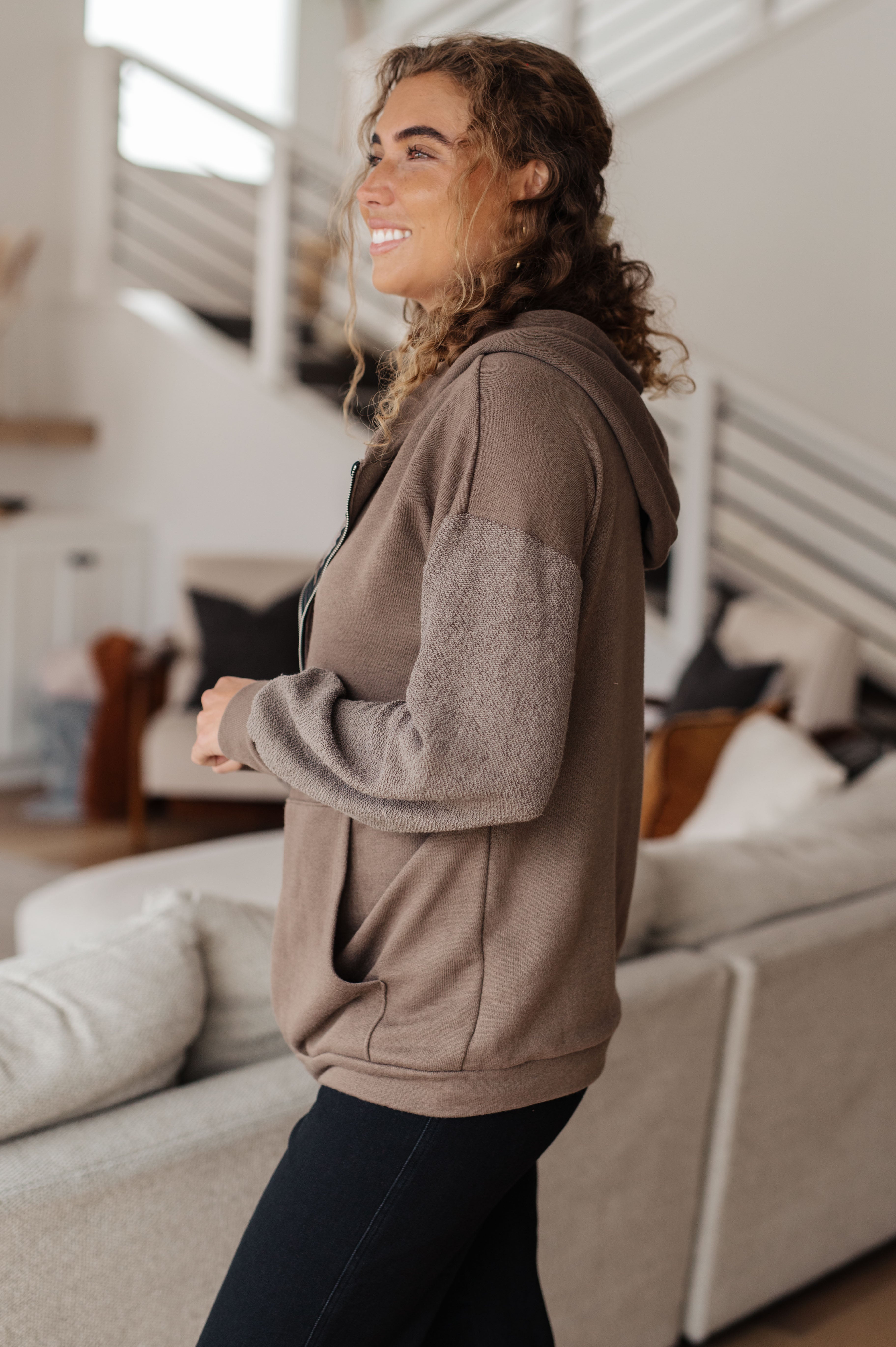 Woman wearing a brown zip-up hoodie over black jeans in a casual indoor setting
